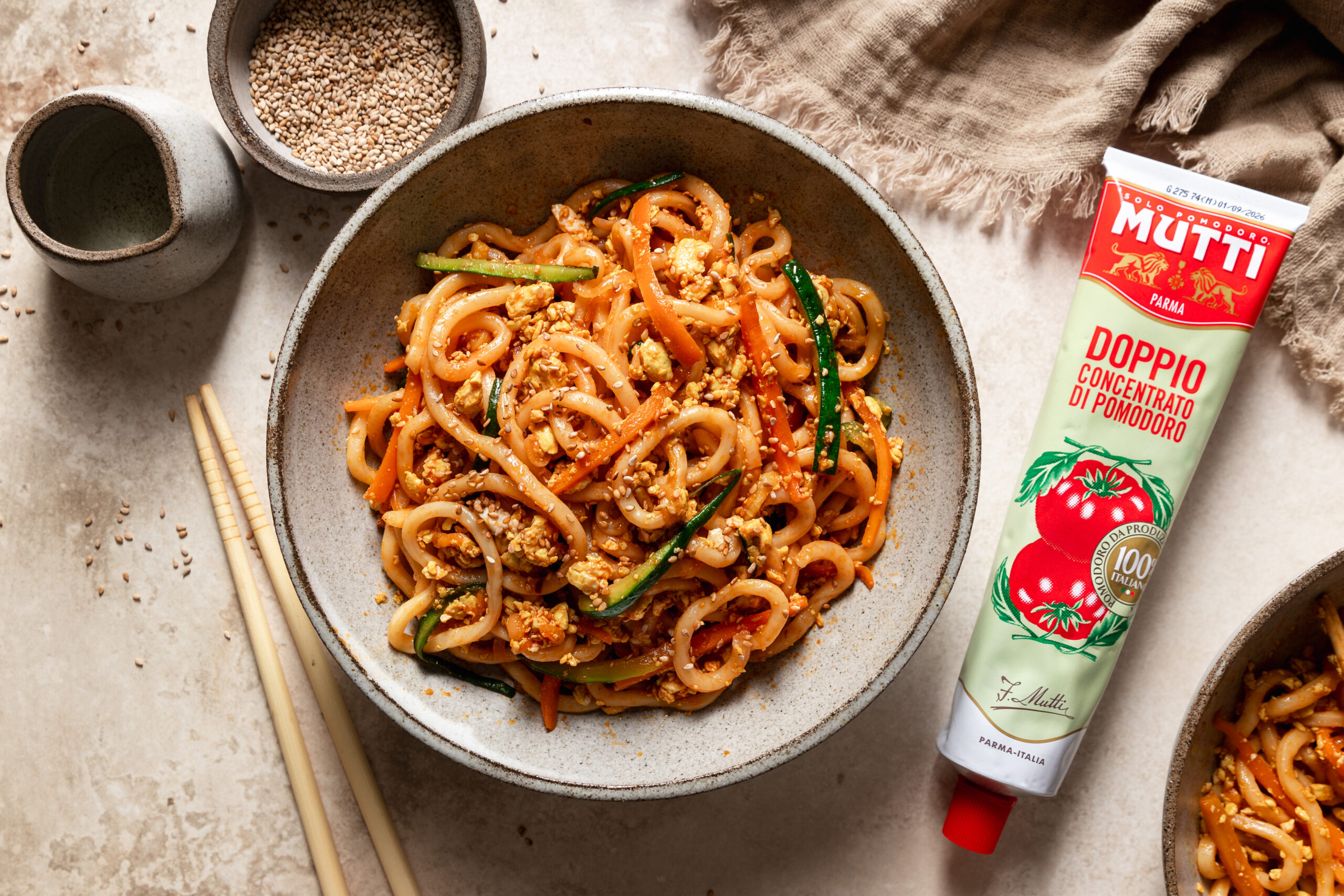 Bowl of udon noodles with vegetables beside a tube of Mutti tomato paste