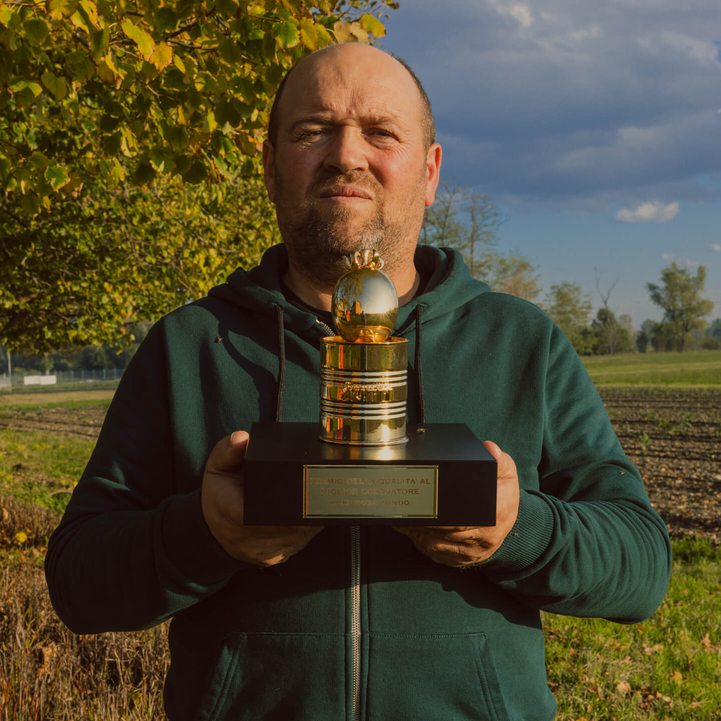 Man holding a golden tomato trophy in a countryside field