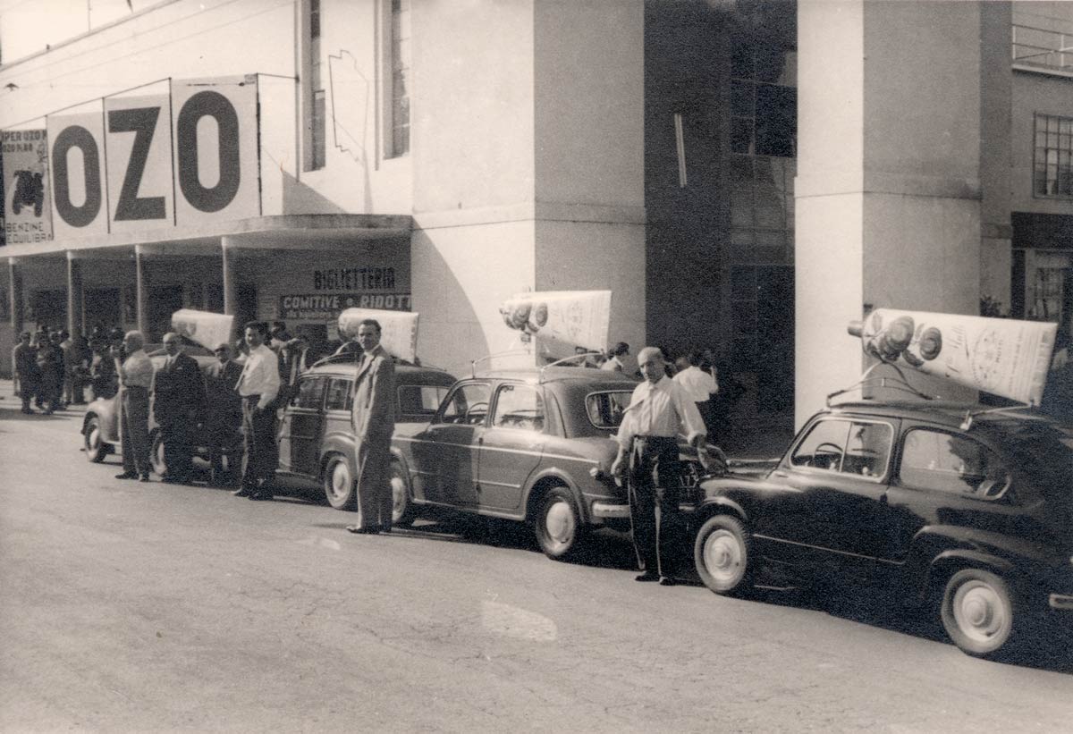 Black-and-white archive photo of vintage cars with rooftop advertising signs