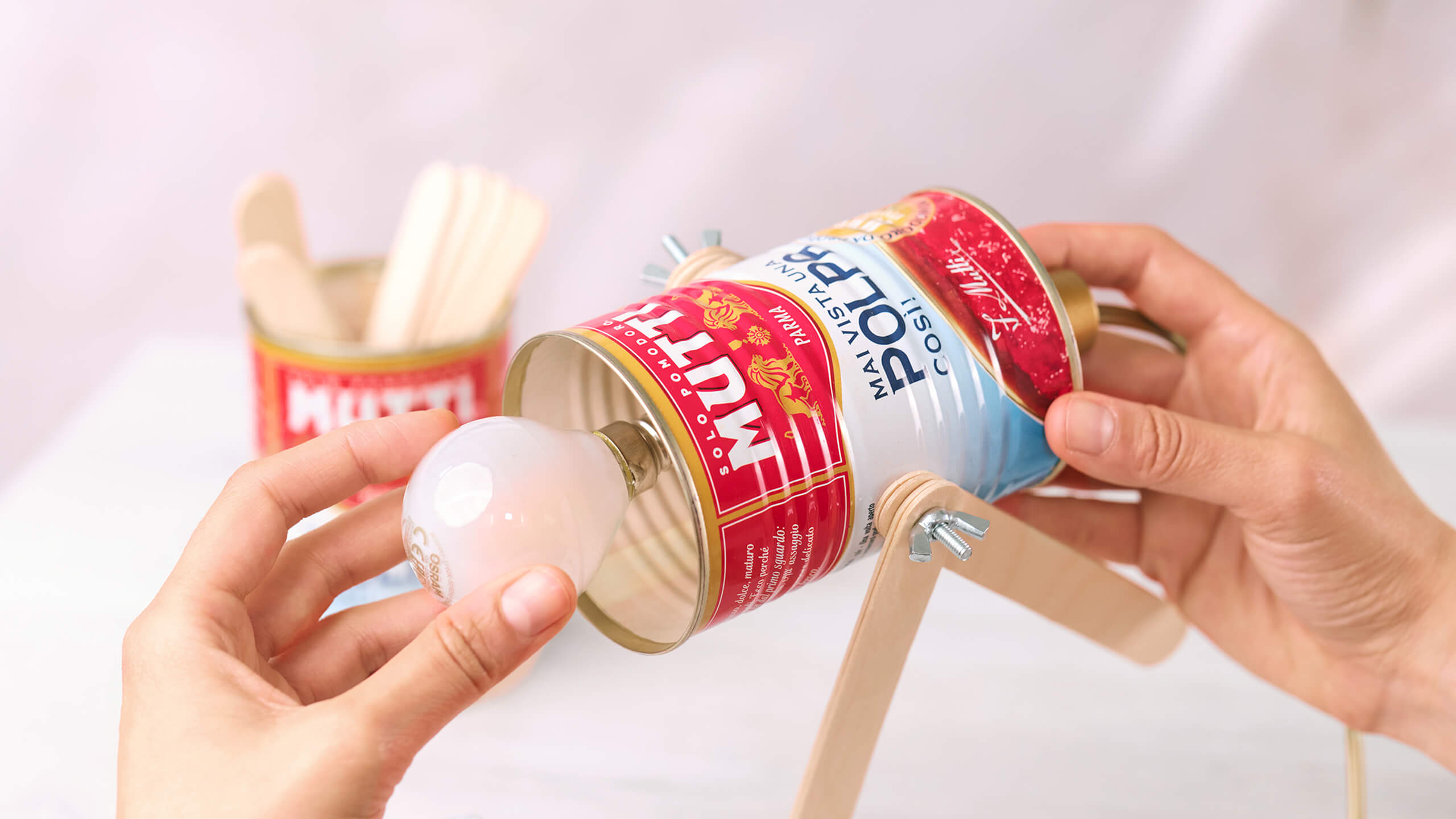 Hands assembling a toy from an empty Mutti can and a light bulb