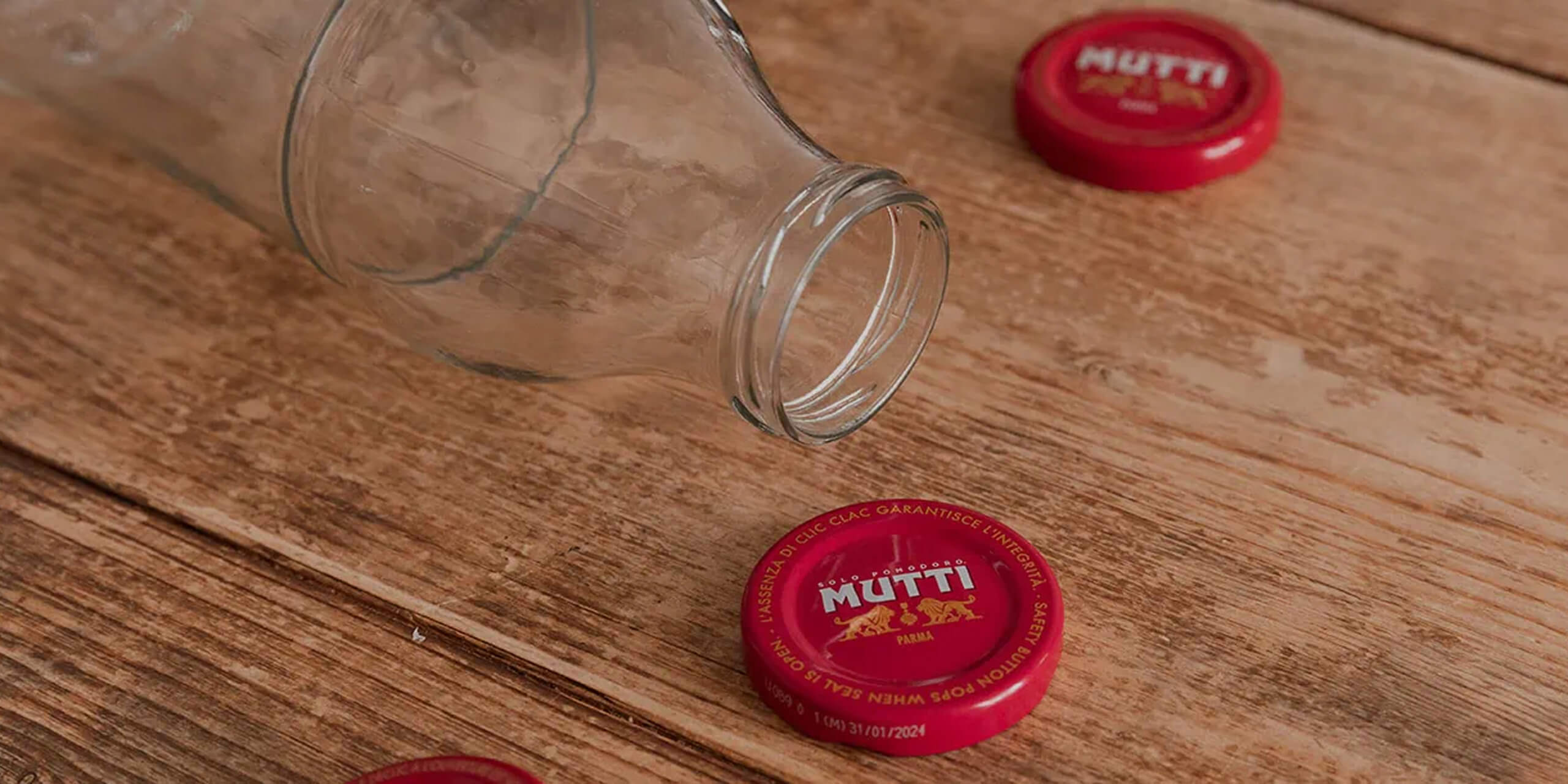 Empty glass bottle beside red Mutti bottle caps on wood