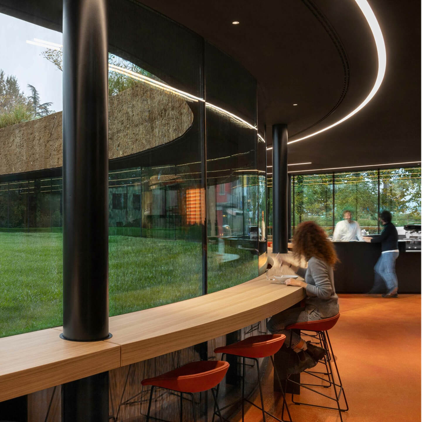 People seated at a curved wooden counter inside a modern glass building
