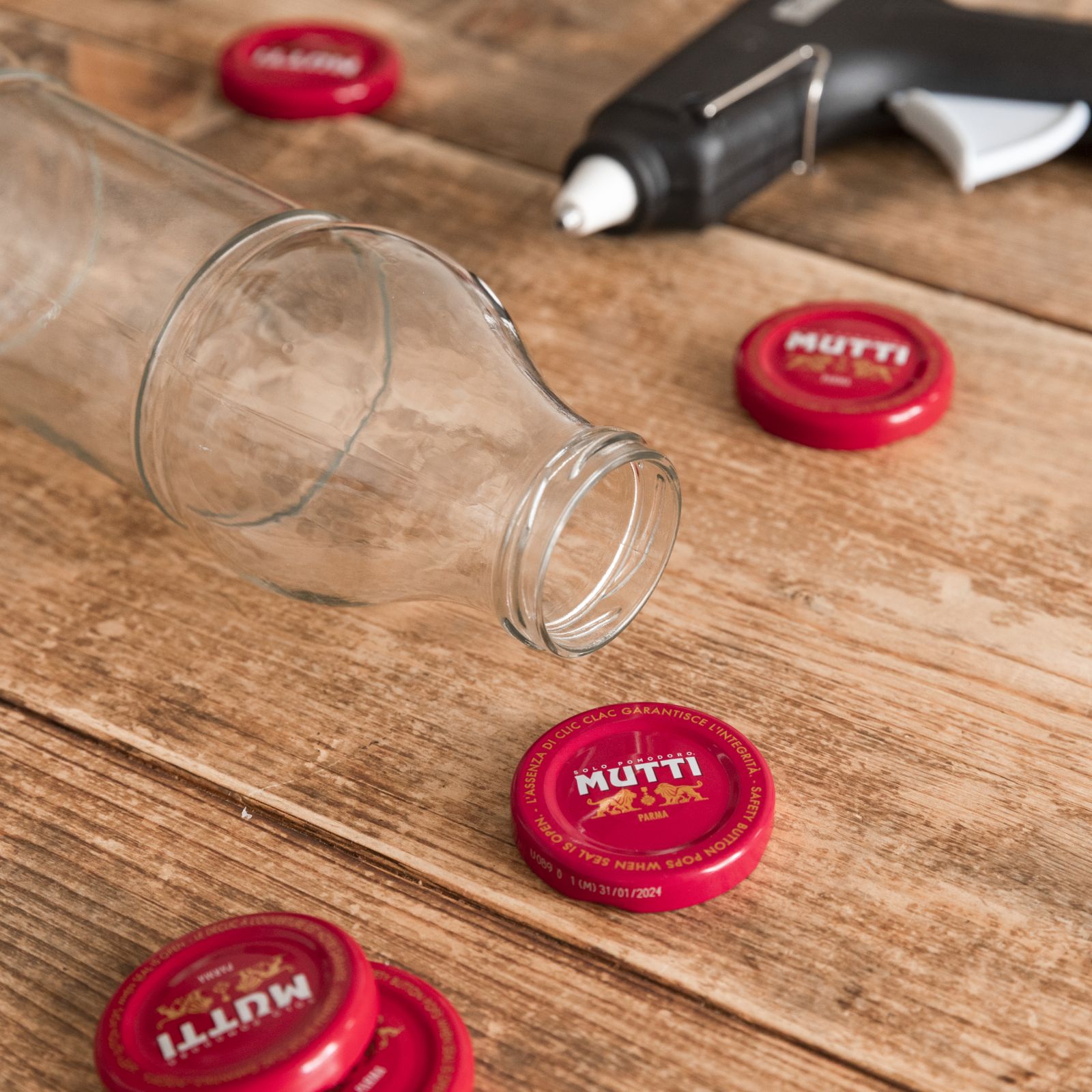 Glass bottle and Mutti caps beside a glue gun for a DIY craft