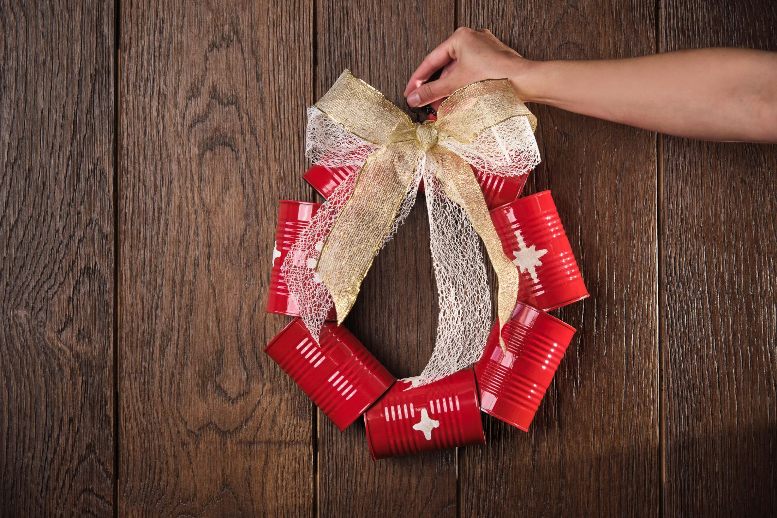 Hand tying a ribbon bow on a wreath made of Mutti tomato cans