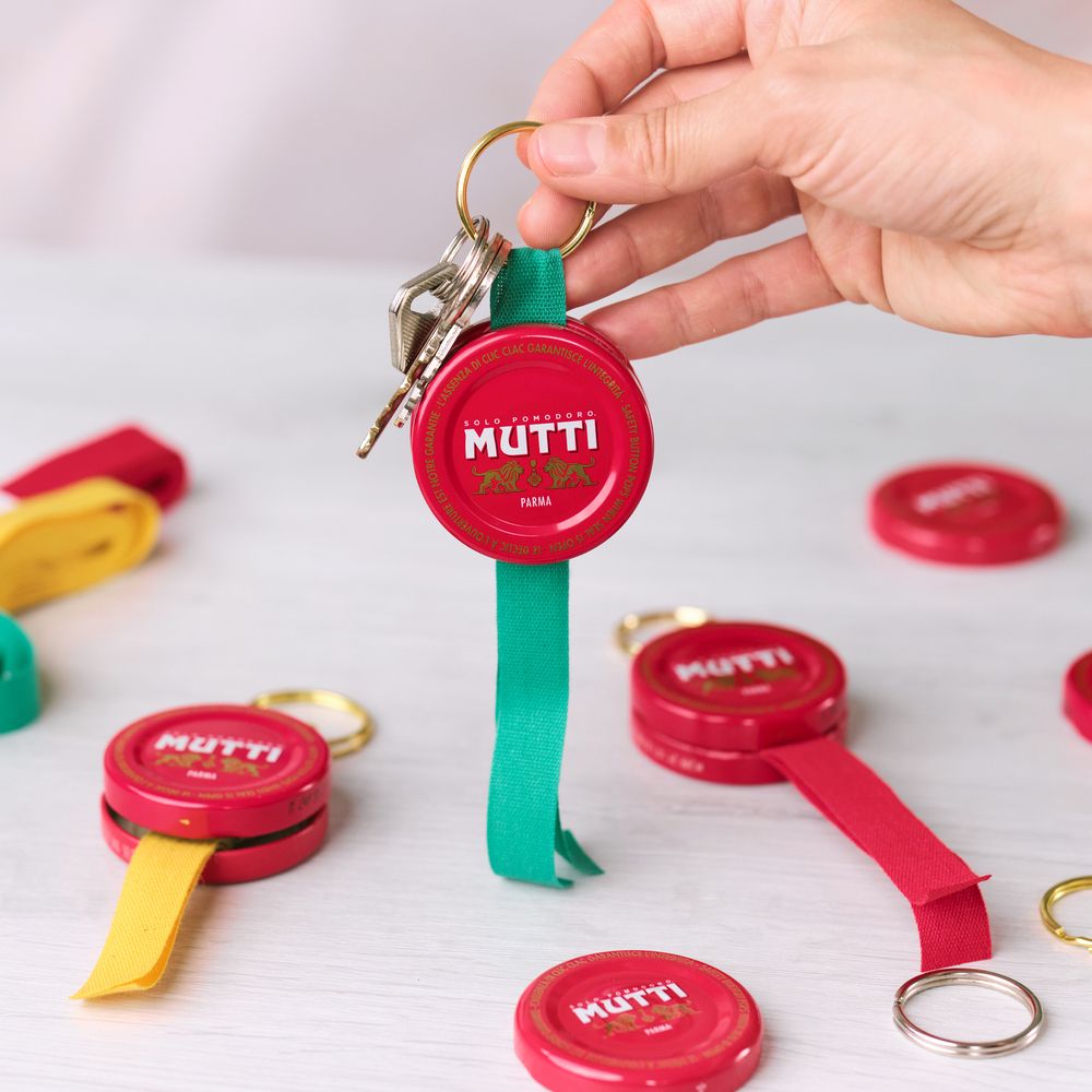 Hand holding a keychain made from a red Mutti Passata bottle cap