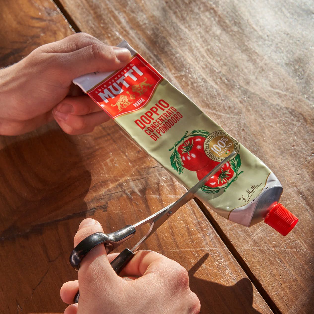 Hands cutting an empty Mutti tomato paste tube with scissors