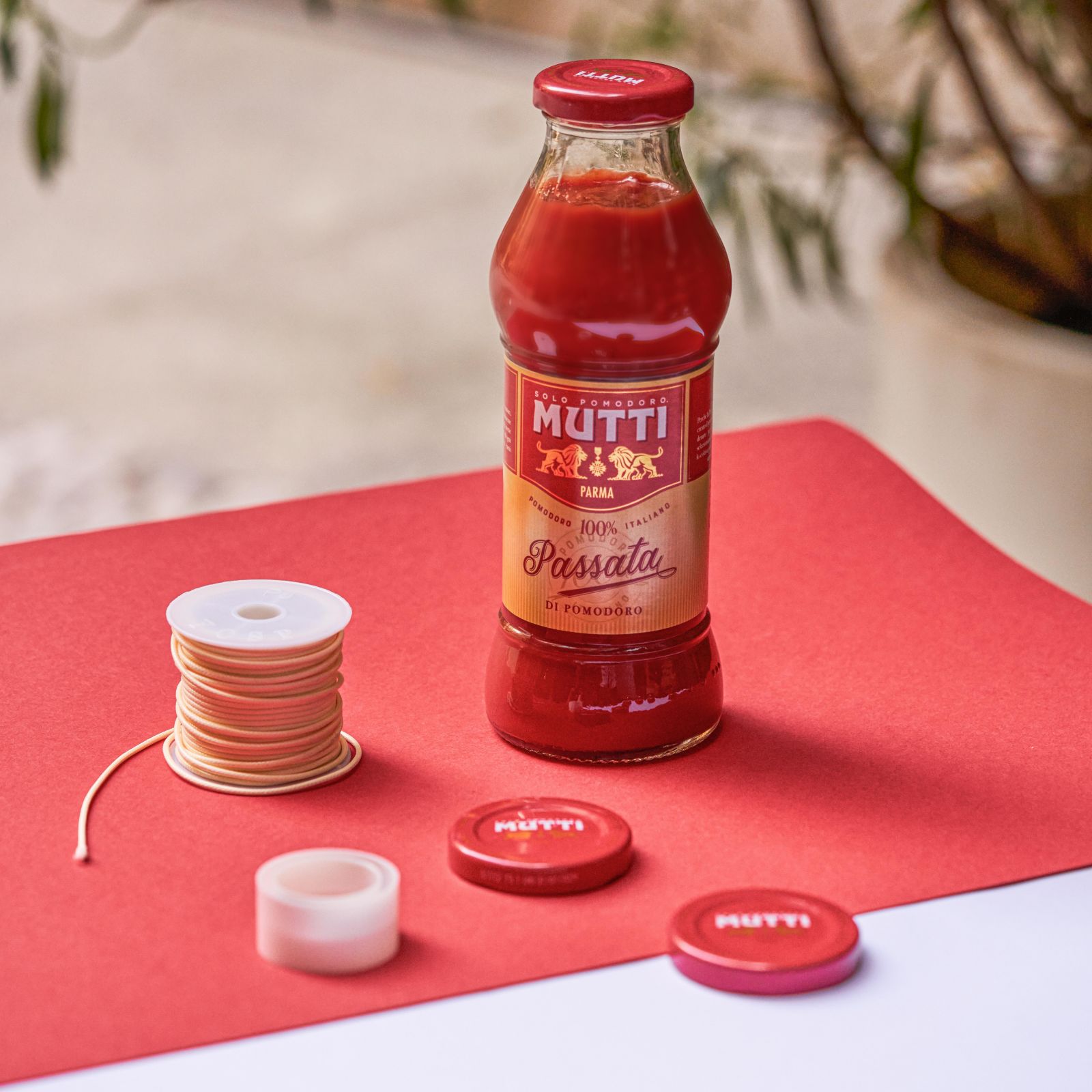 Mutti Passata bottle beside caps and string on a red background