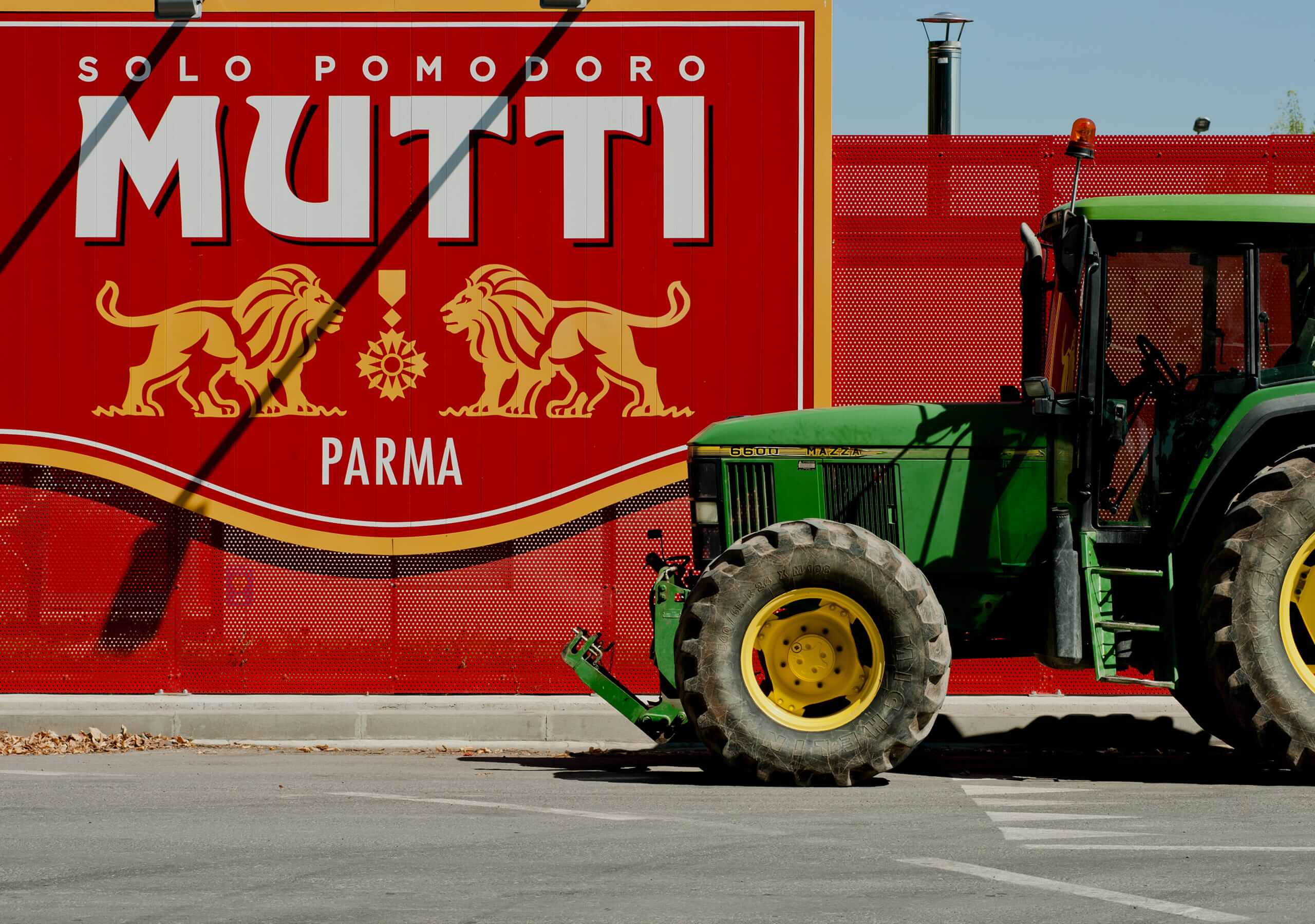 Green tractor driving past a large Mutti Parma billboard