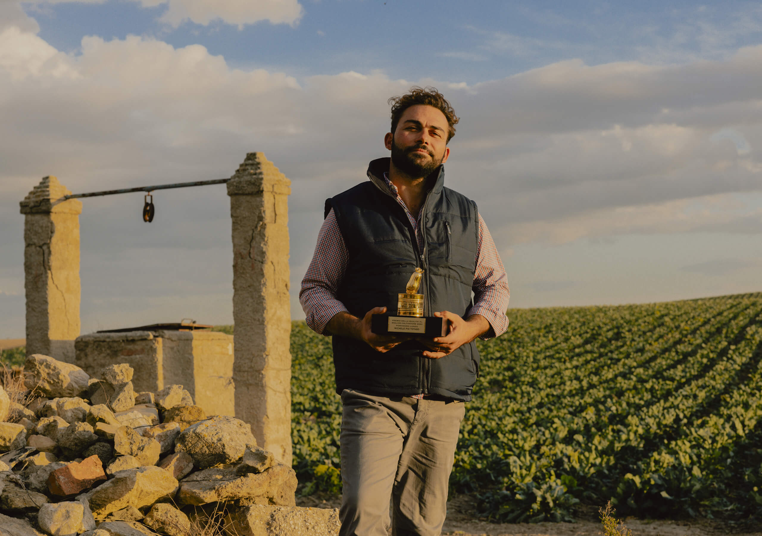 Farmer holding the golden Pomodorino d'Oro trophy in a tomato field at sunset