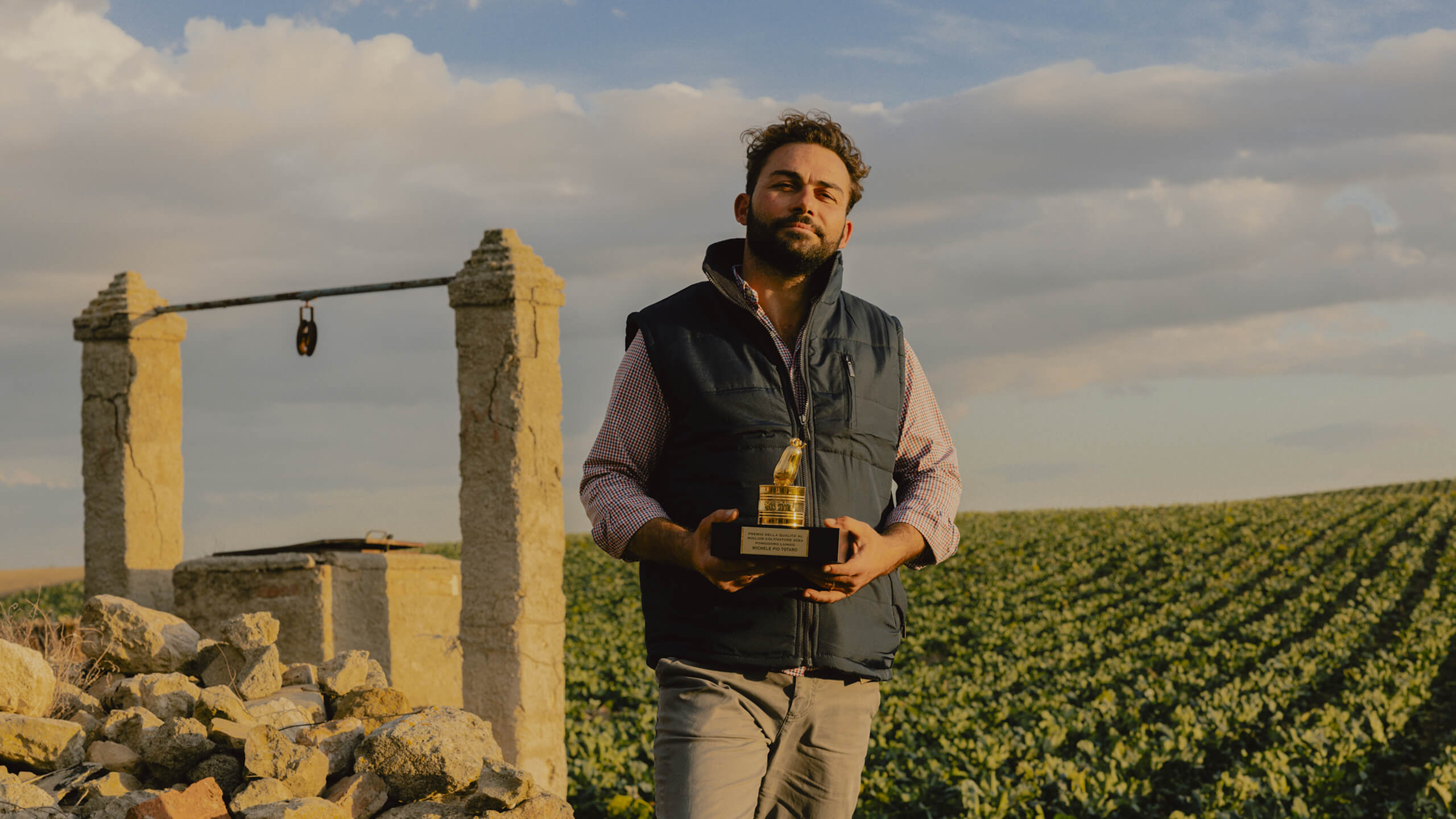 Man holding a golden tomato award trophy in a field at sunset