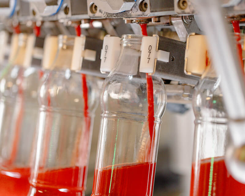 Glass bottles filling with red tomato purée on the bottling line