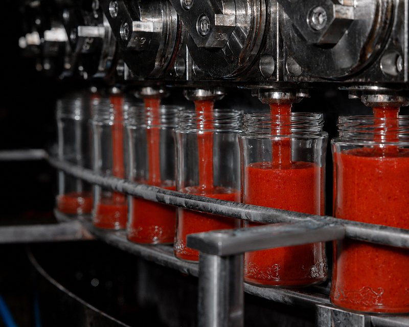 Glass jars of pasta sauce being sealed on the filling line