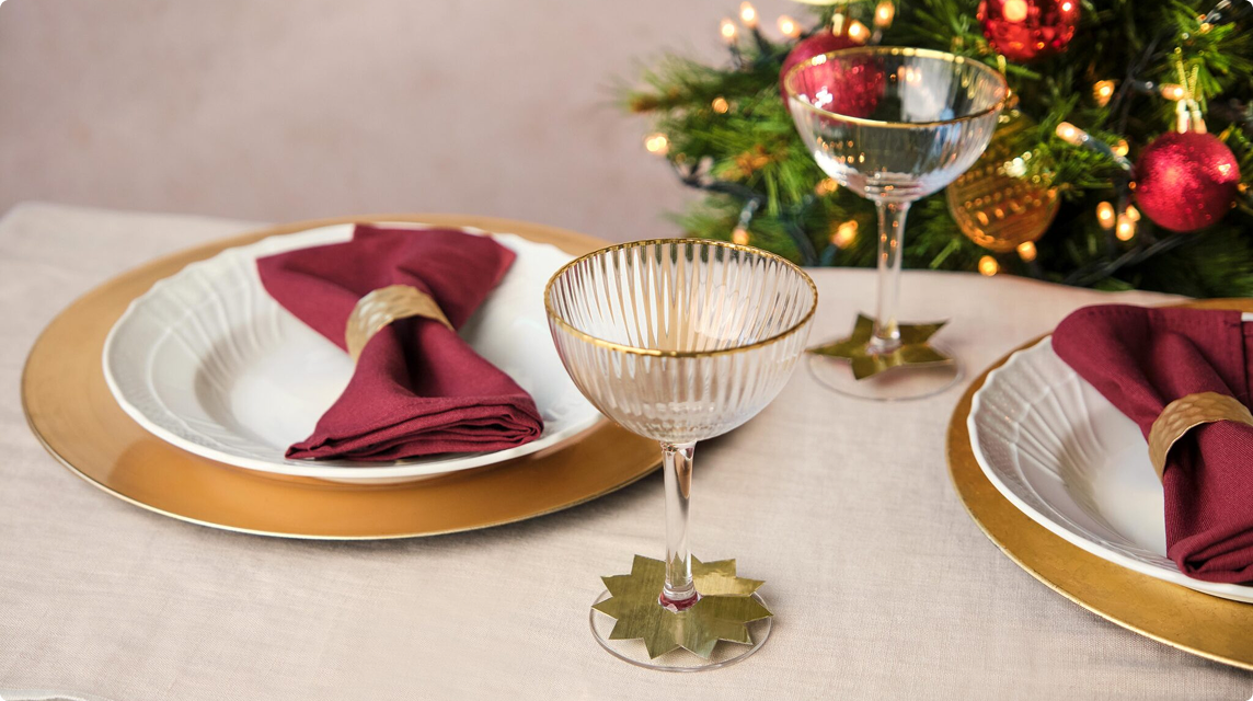 Gold-rimmed table setting with napkins and glasses by a Christmas tree