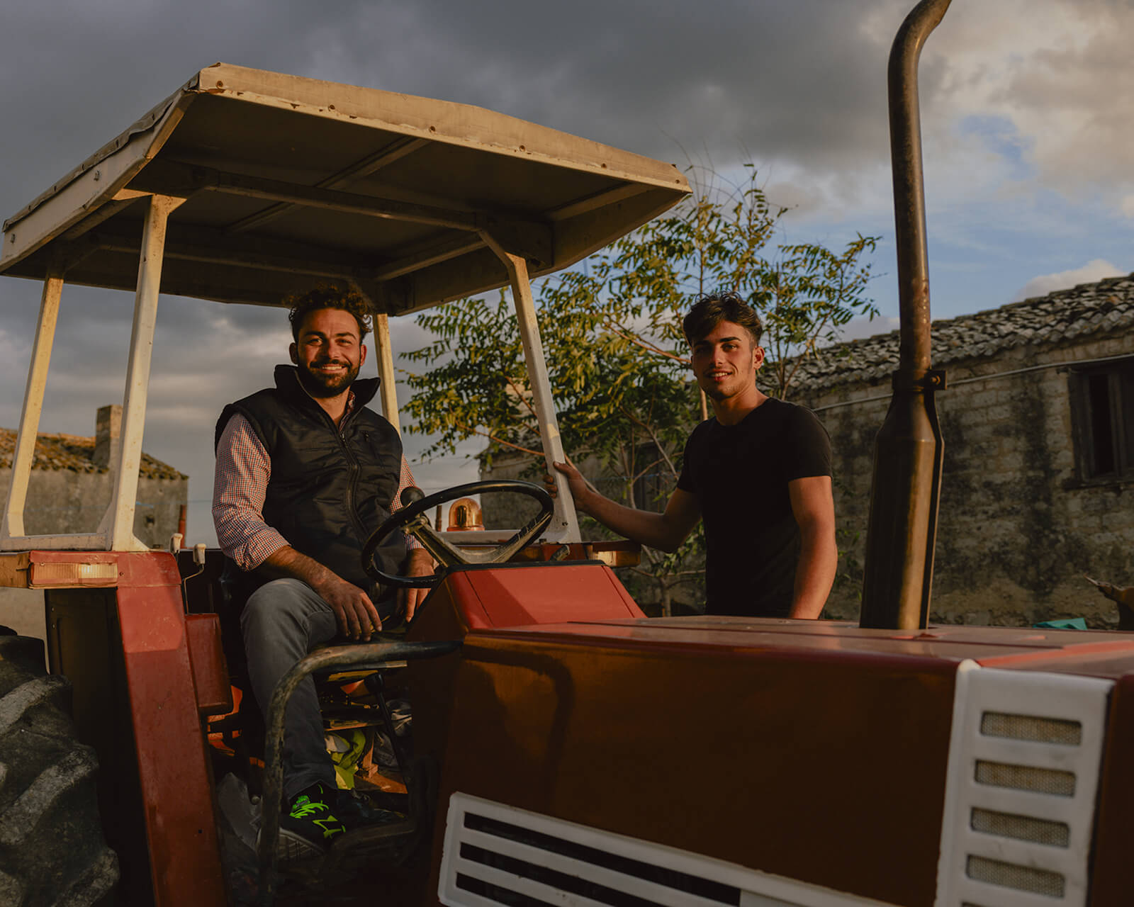 Two farmers sitting on a vintage tractor at sunset