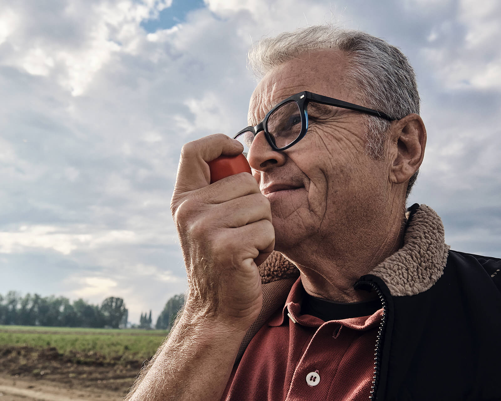 Mutti farmer smelling a ripe tomato in the field