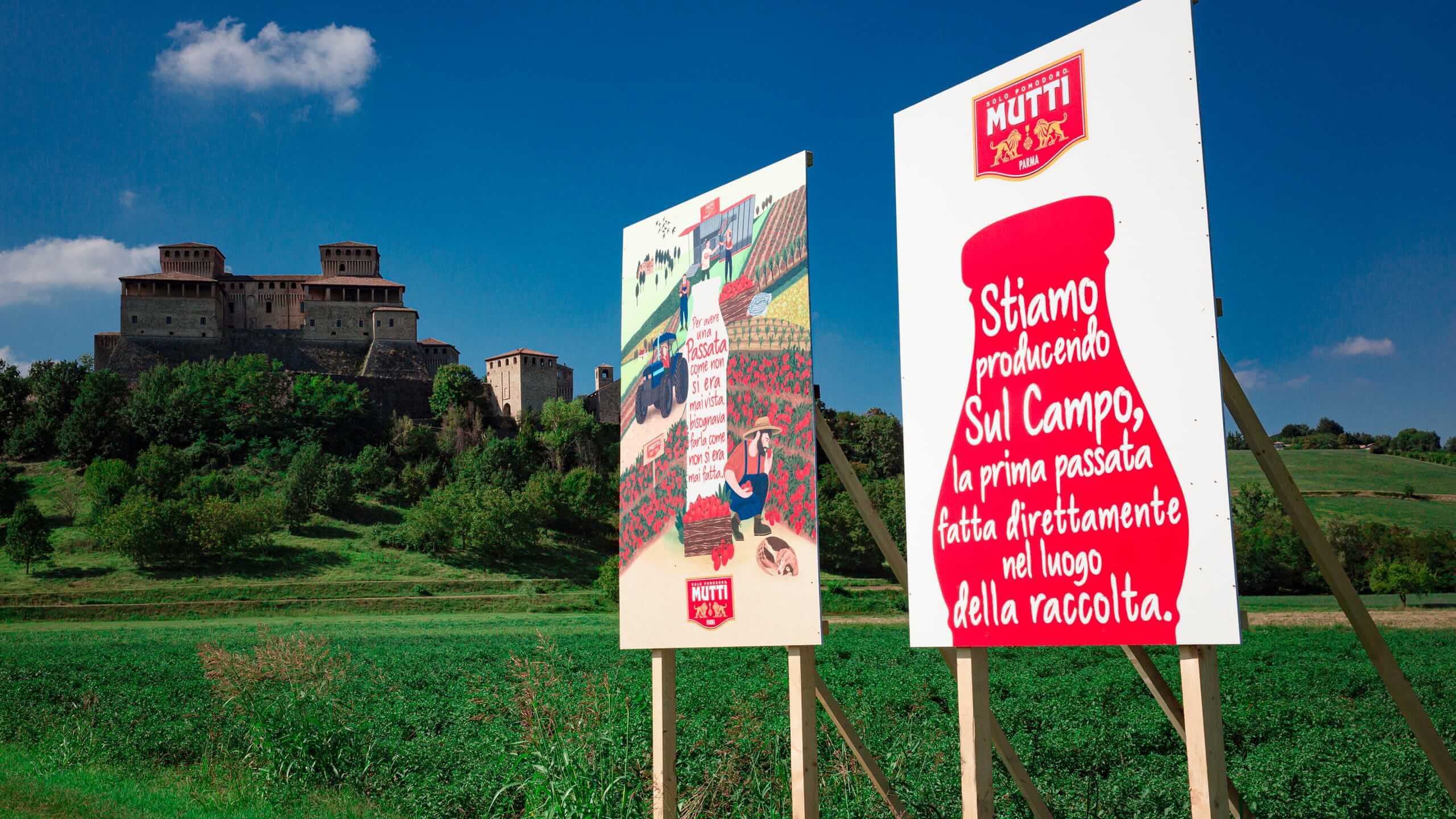 Mutti signboards in a tomato field below a hilltop castle
