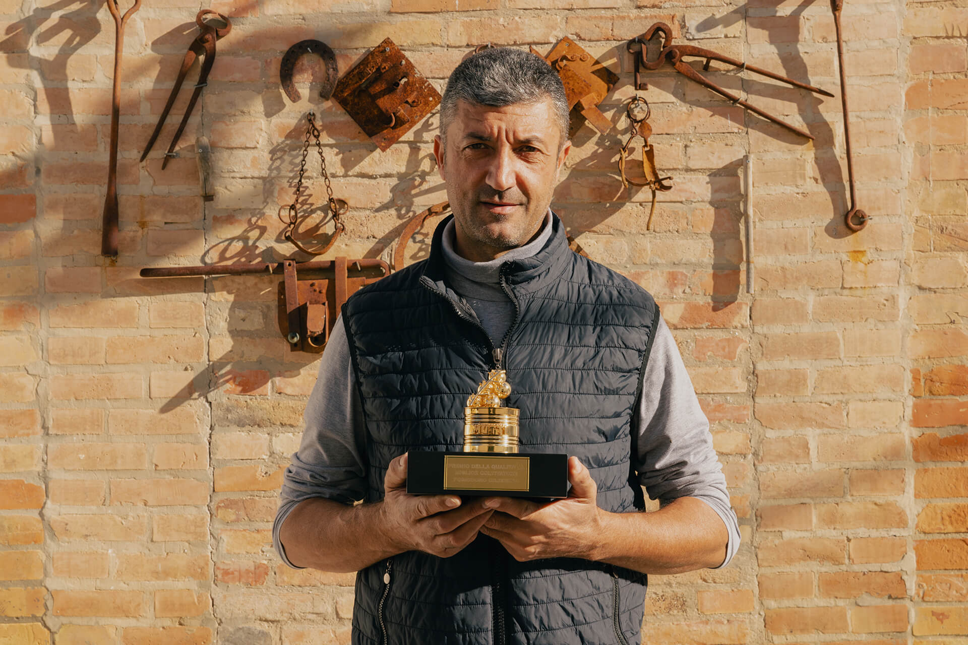 Mutti farmer holding the Pomodorino d'Oro trophy against a rustic wall