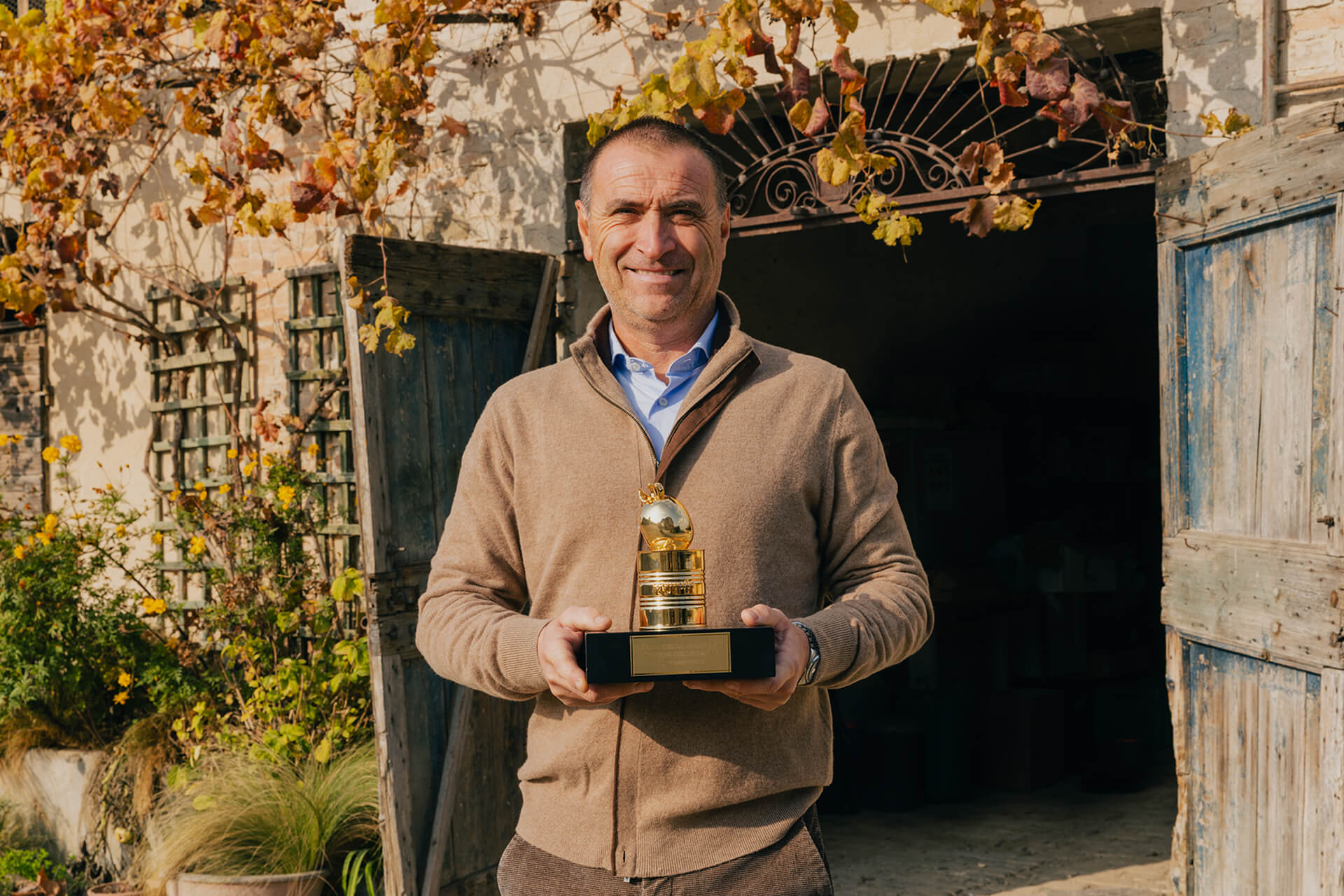 Farmer holding the golden Pomodorino d'Oro trophy outside a stone farmhouse