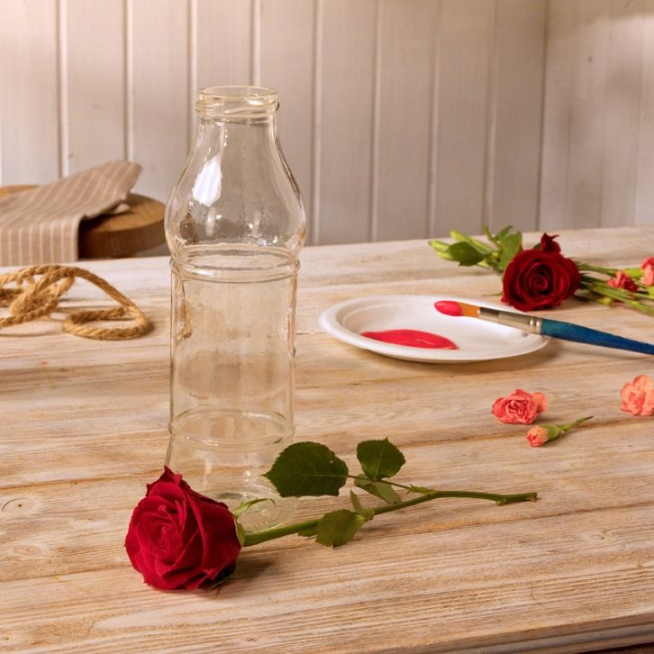 Empty glass bottle beside red roses and a dish of red paint