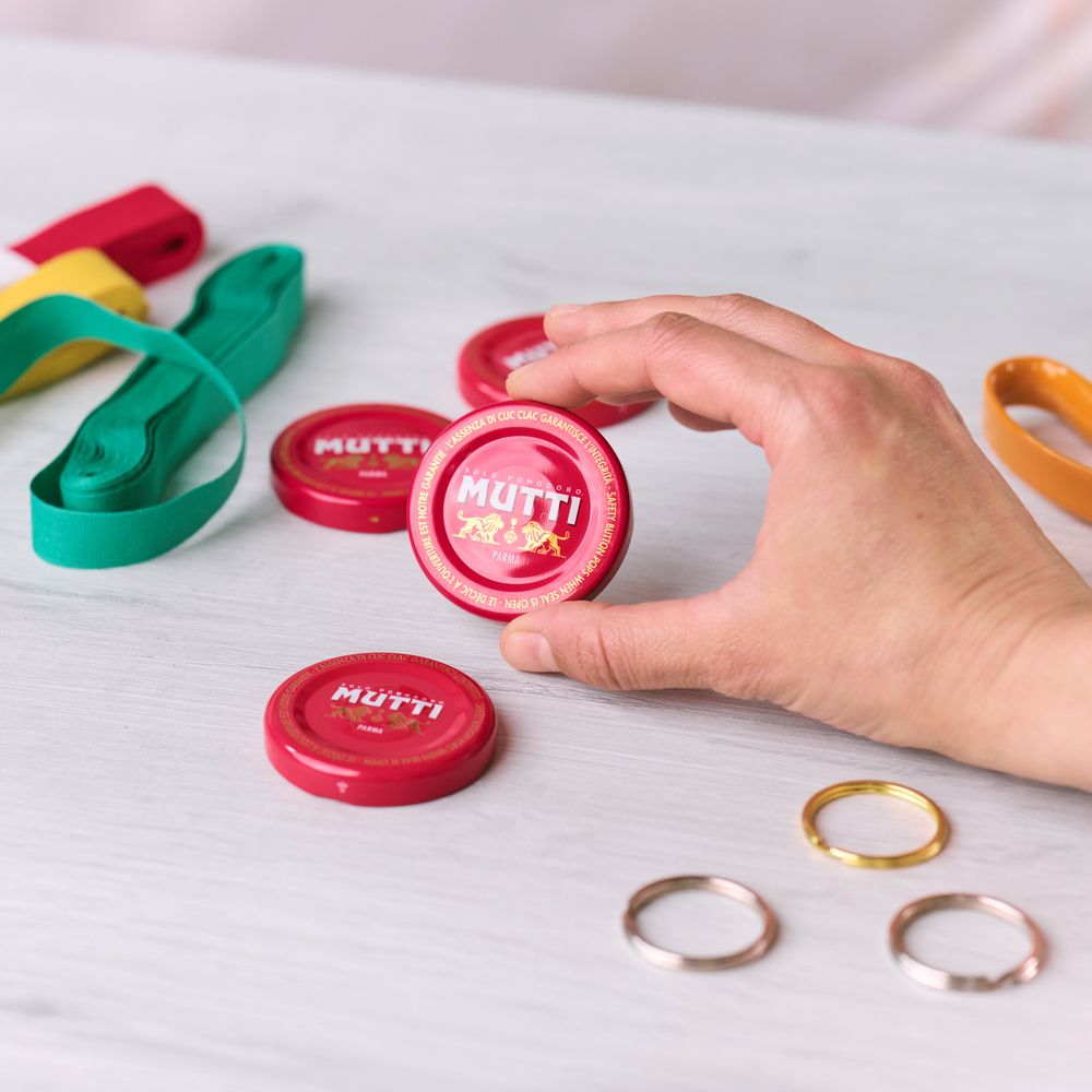 Hand holding two red Mutti Passata bottle caps and ribbons