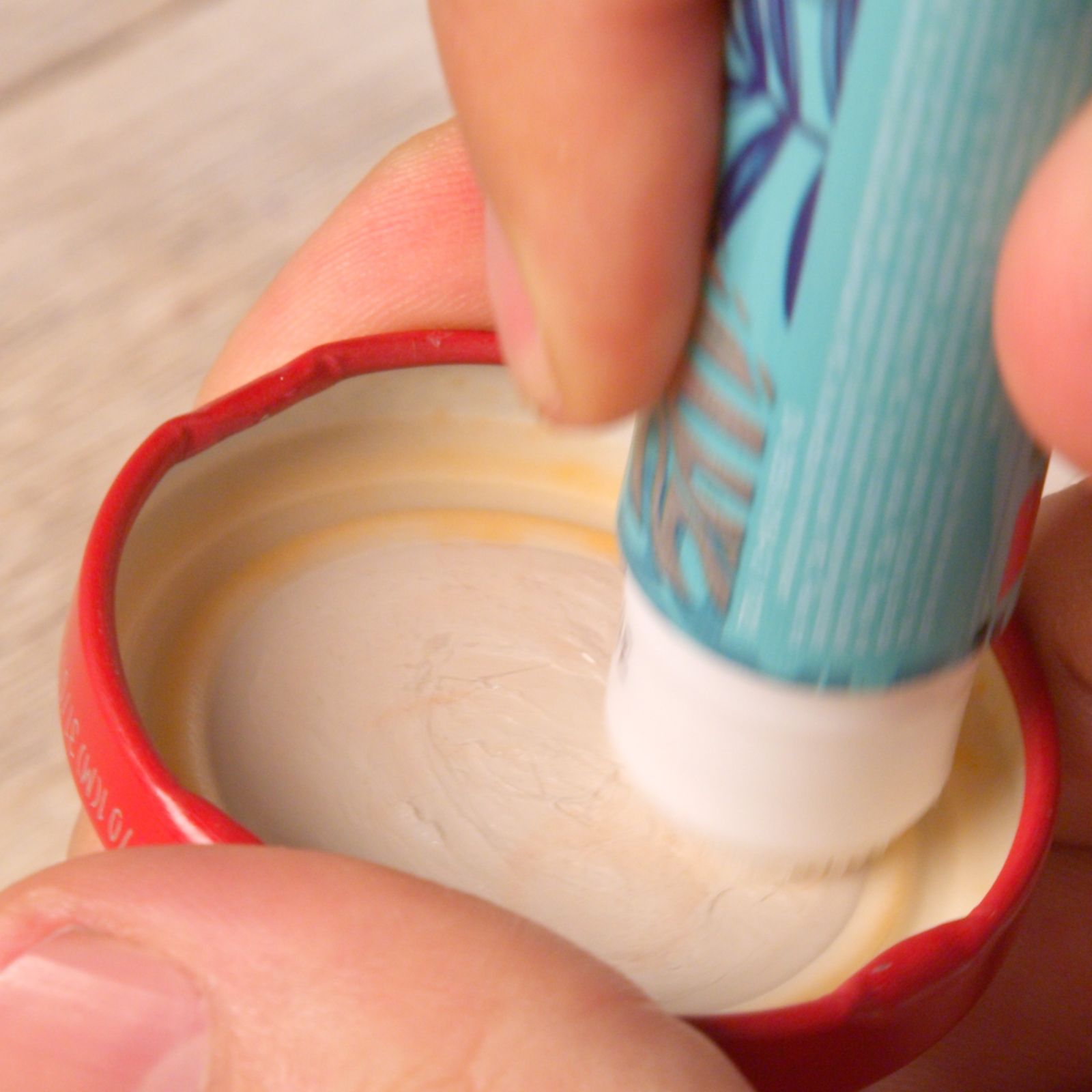 Hand gluing a printed illustration inside a red bottle cap