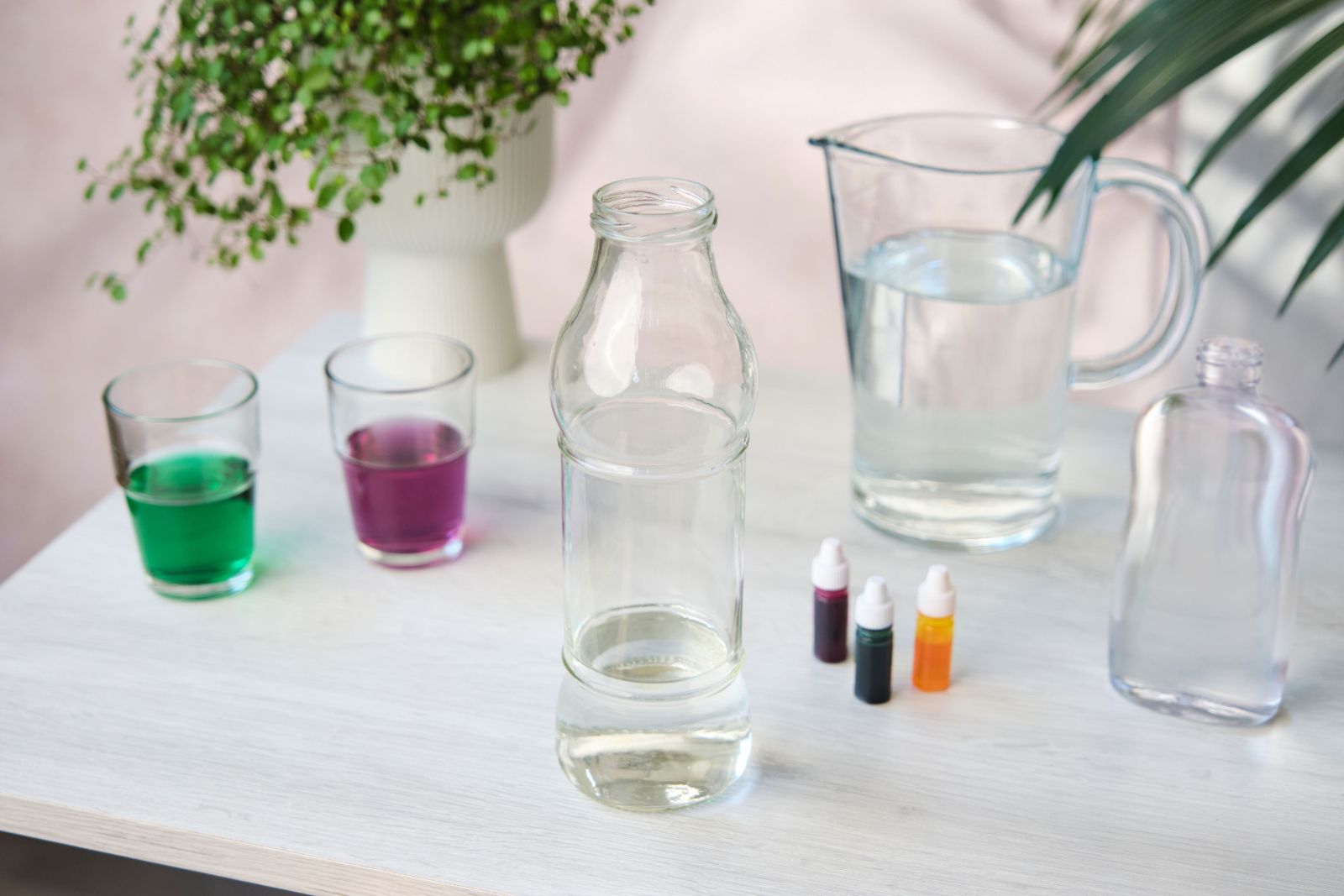 Empty glass bottle beside a water pitcher for a DIY lava lamp