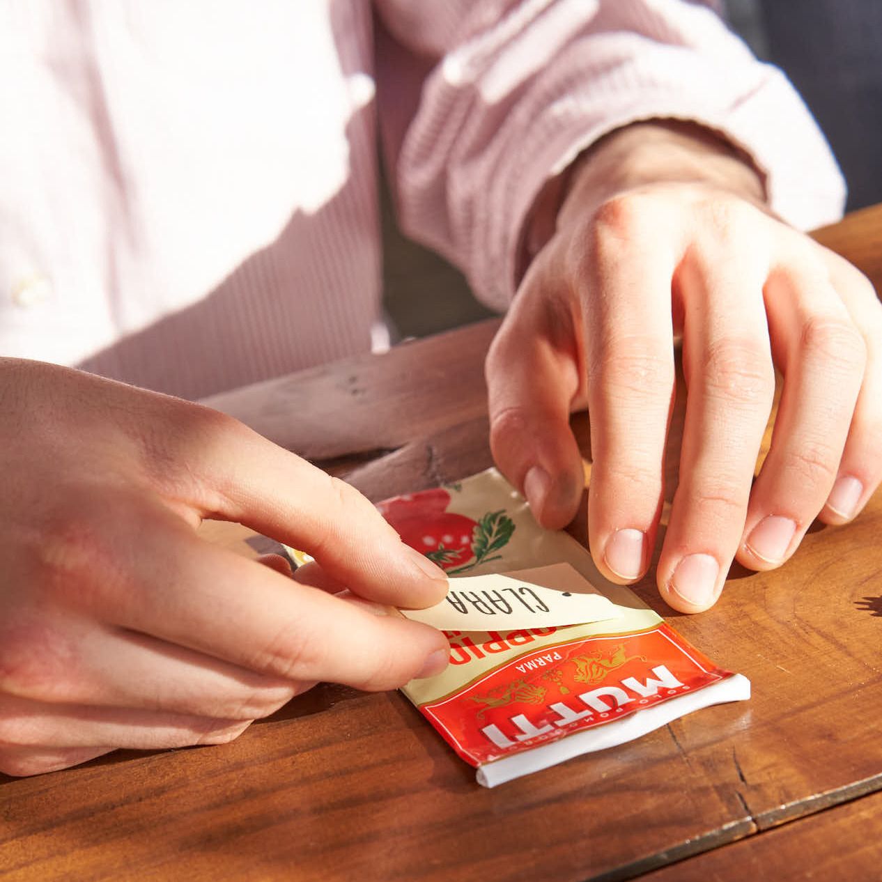Hands peeling a handwritten name tag off a Mutti tomato paste tube
