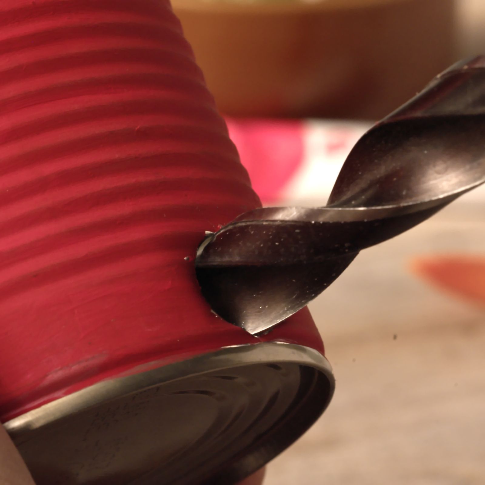 Drilling a hole into a red painted tin can