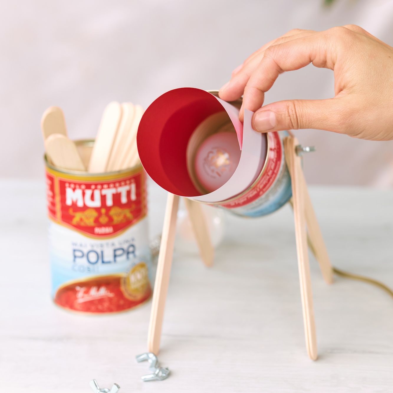 Hand wrapping a red paper lampshade around a Mutti can lamp
