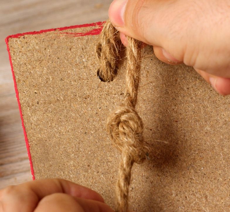 Hands tying jute twine into a knot on a canvas panel