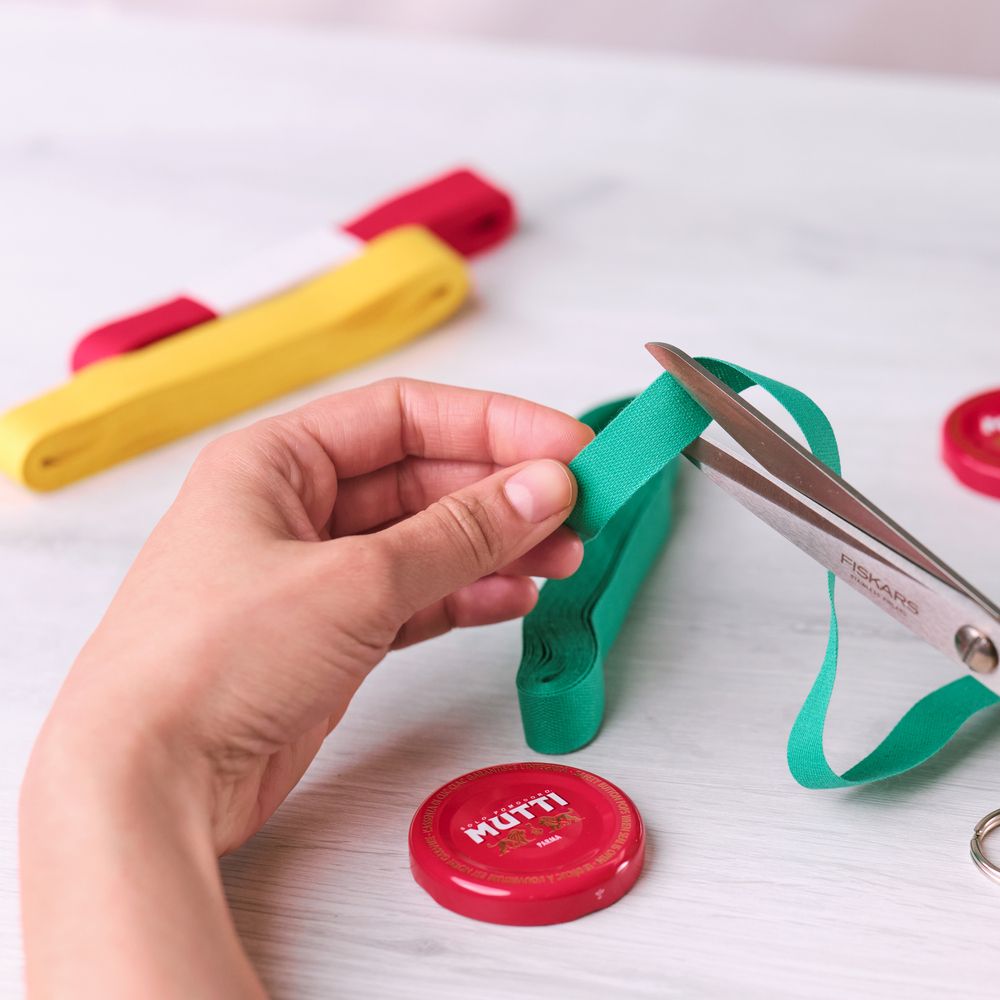Cutting a green ribbon with scissors beside a Mutti bottle cap