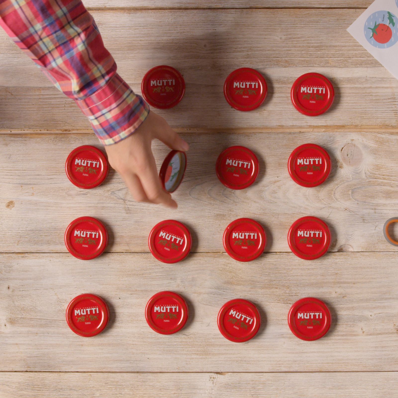 Hand playing a memory game with Mutti bottle caps on a table
