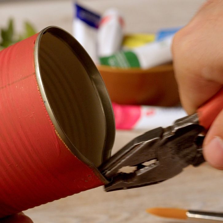 Cutting an opening into a red painted tin can with pliers