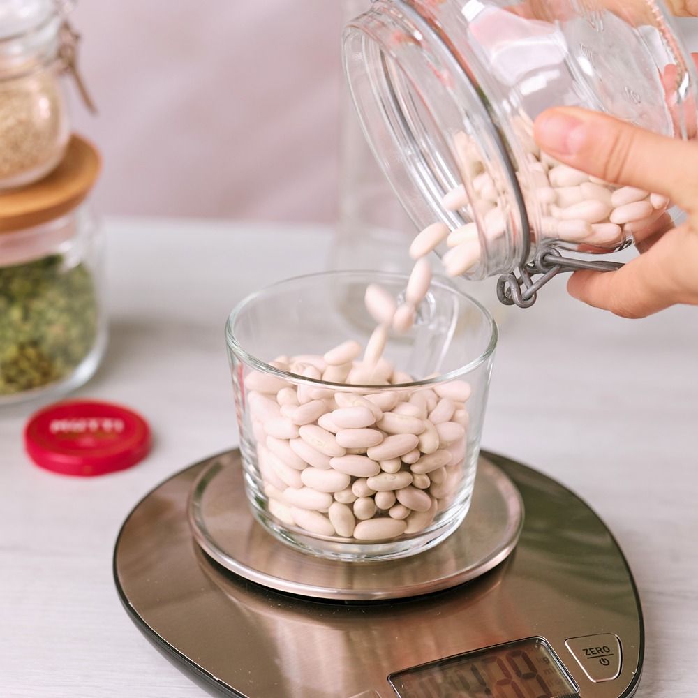 Hand pouring dried white beans into a bowl on a kitchen scale