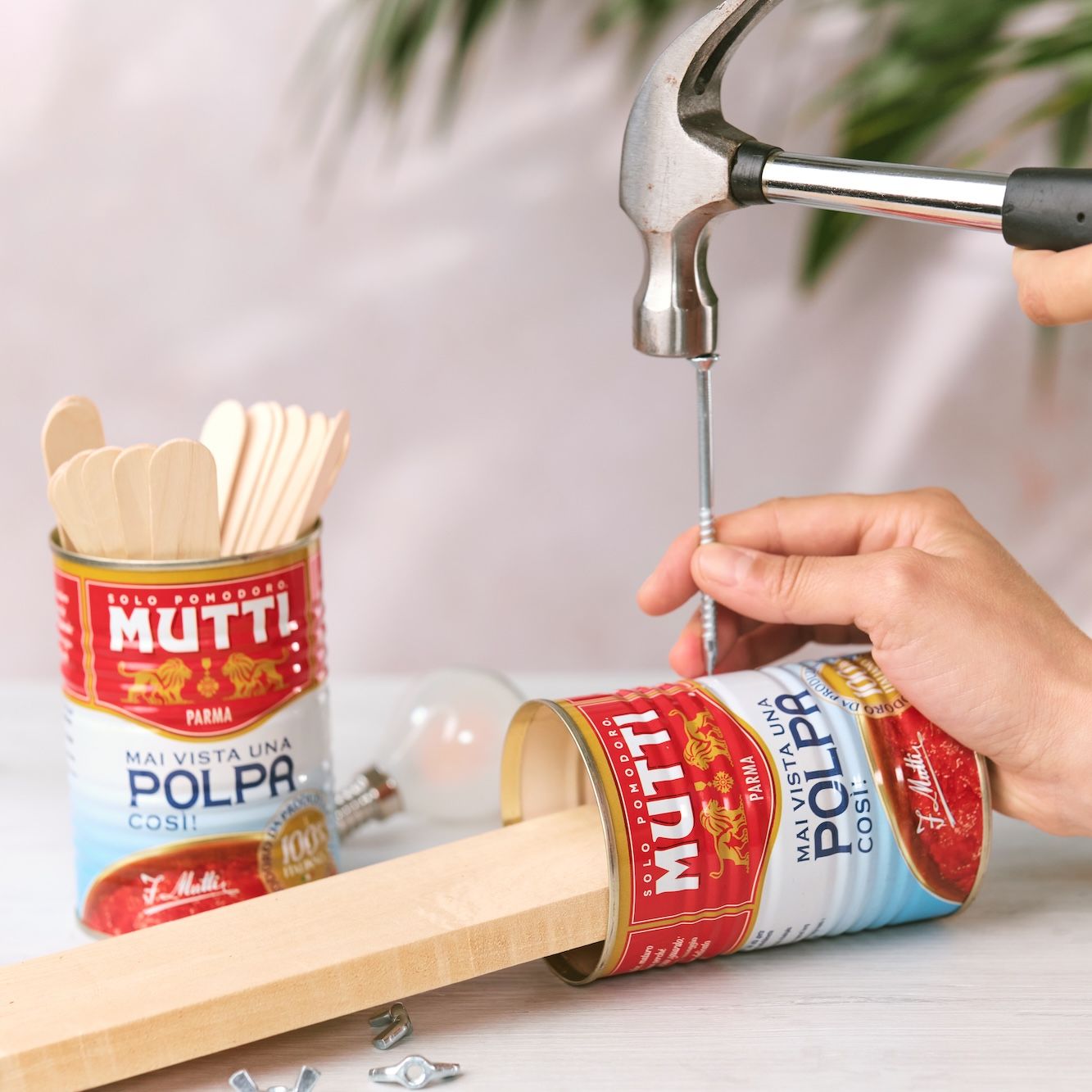 Hammering a nail into a wooden stick beside a Mutti Polpa can