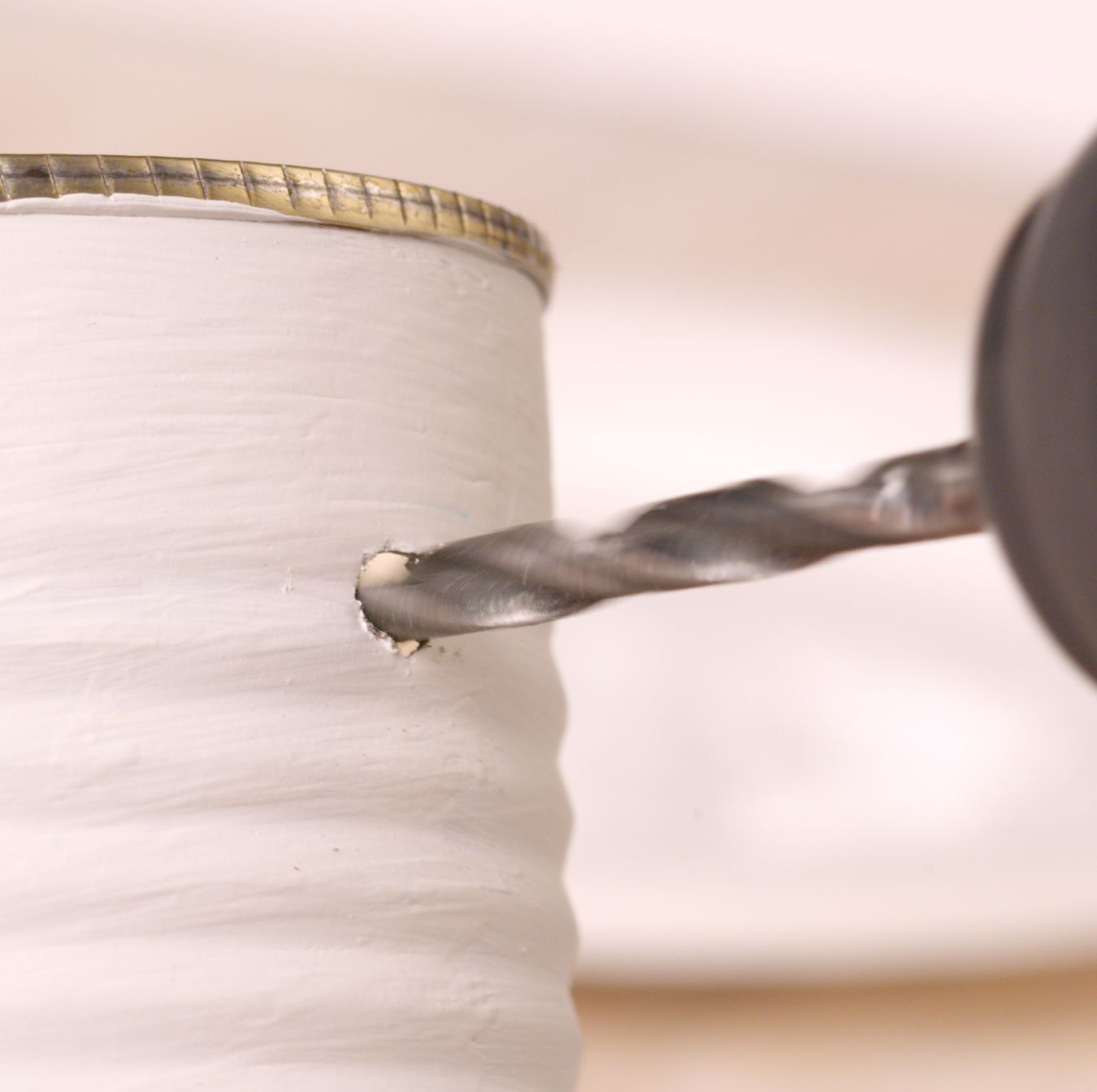 Drill boring a hole into a white-painted can