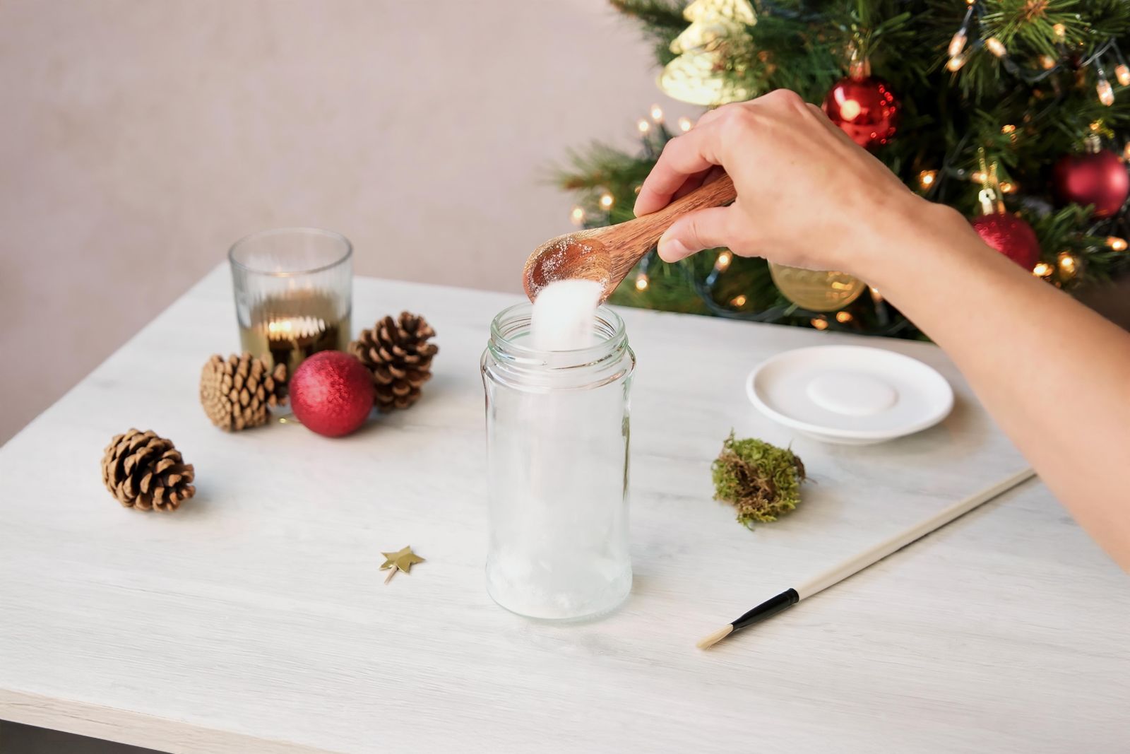 Spooning white sugar into a glass jar for a snow effect