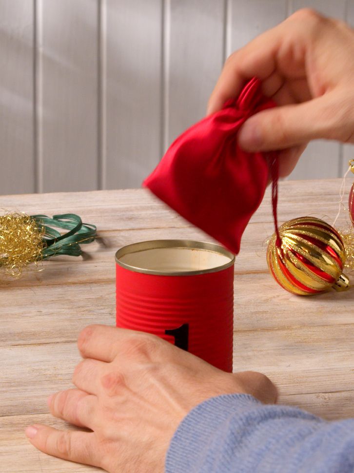 Hand placing a small red gift pouch into a numbered advent calendar can