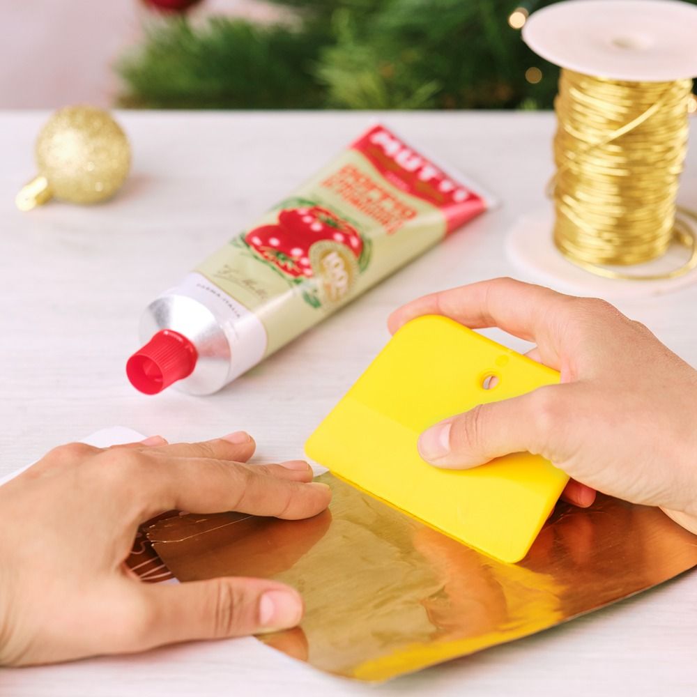 Flattening opened tomato paste tube material with a yellow spatula