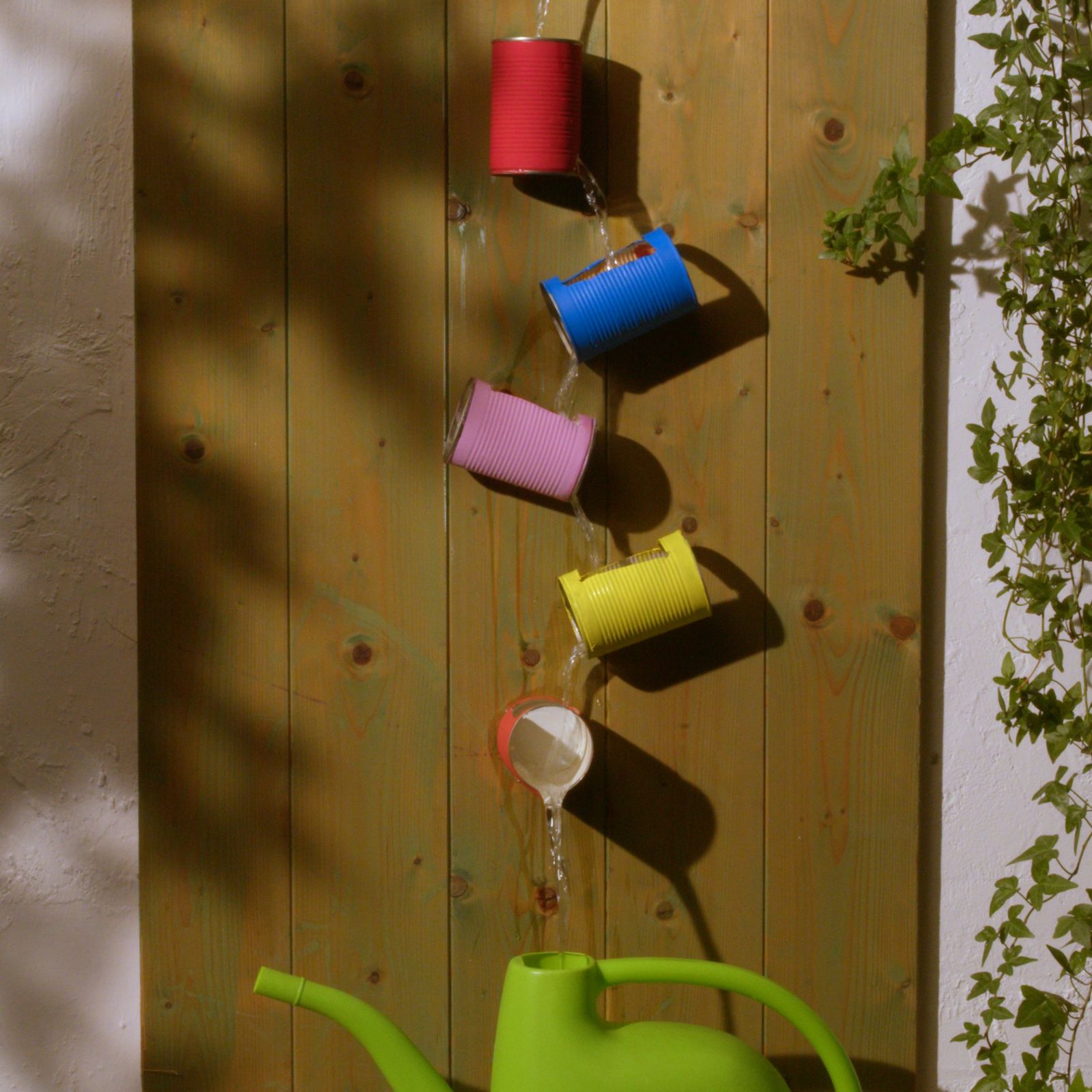 Five painted tin cans forming a rain-saver chain on a wooden fence