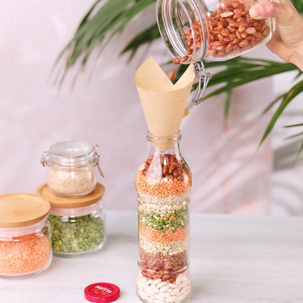 Hand layering dried pulses into a glass bottle with a paper funnel