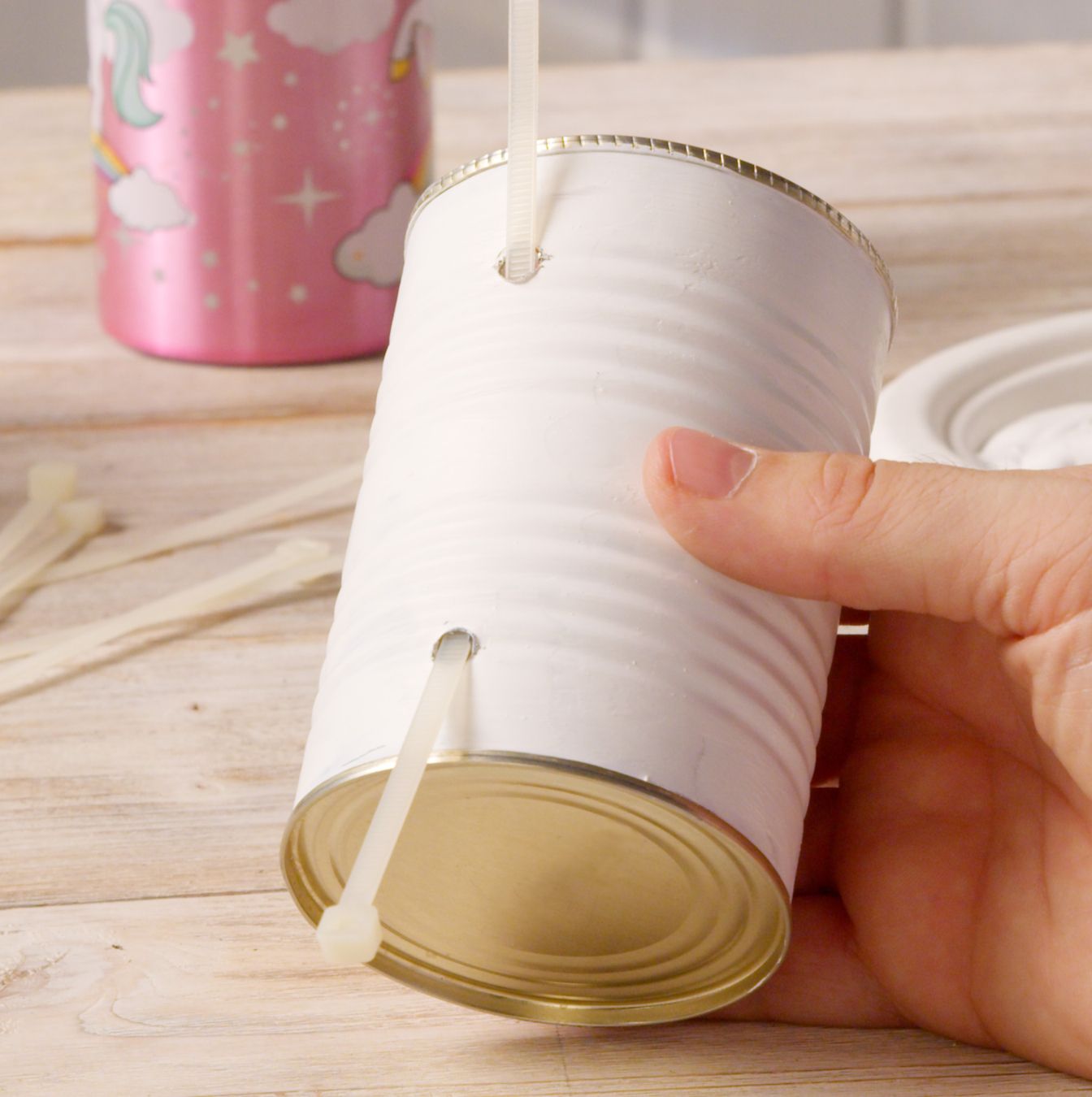 Hand threading a cable tie through holes in a white can