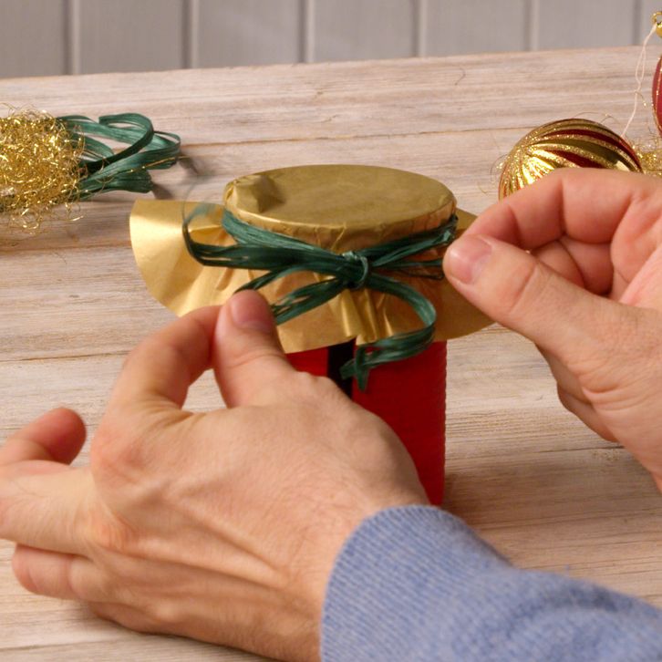 Hands tying a gold fabric circle onto a can with green ribbon