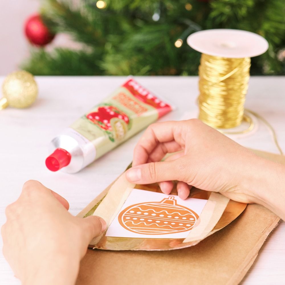 Placing a paper bauble stencil onto gold tube material