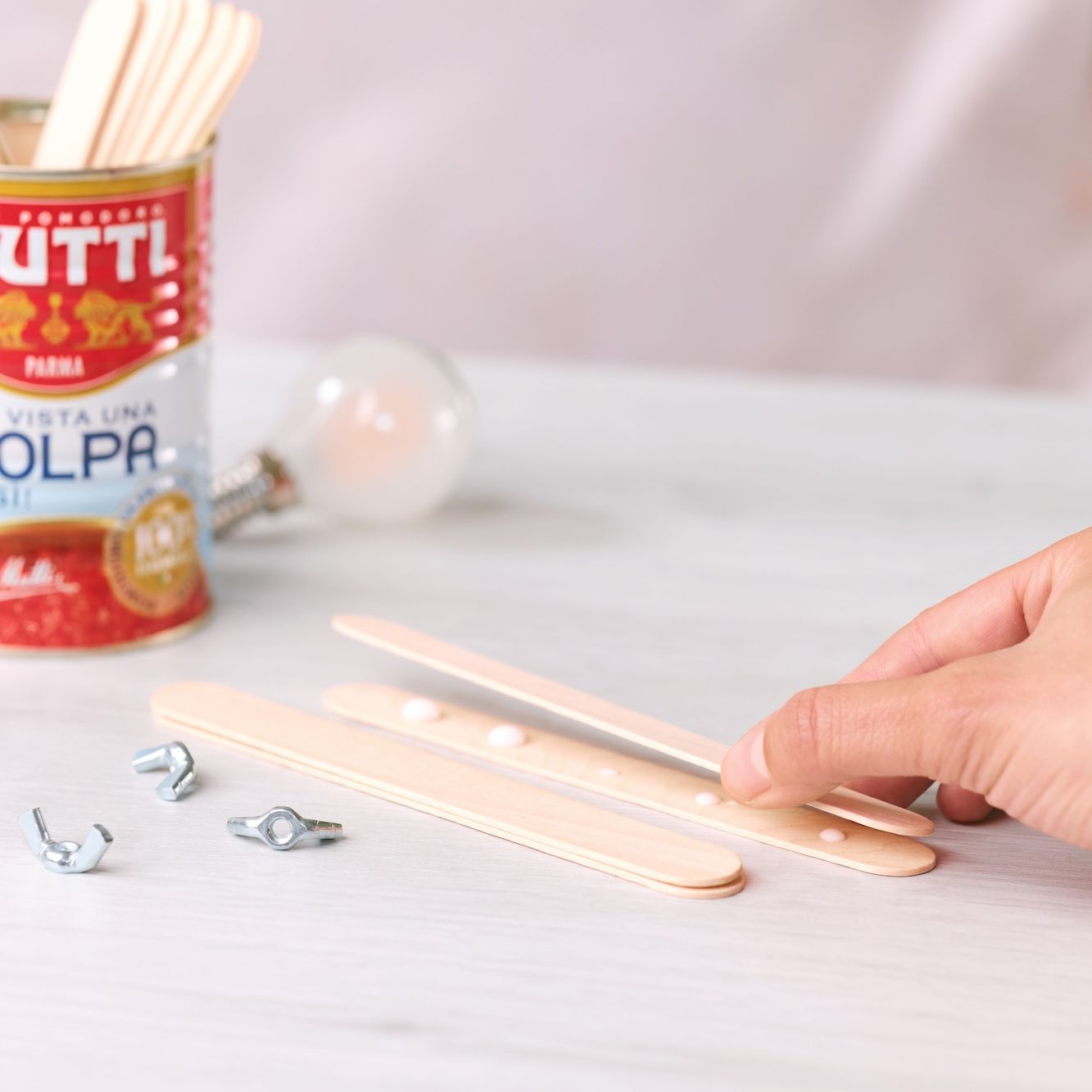 Hand joining wooden craft sticks in pairs for a lamp base