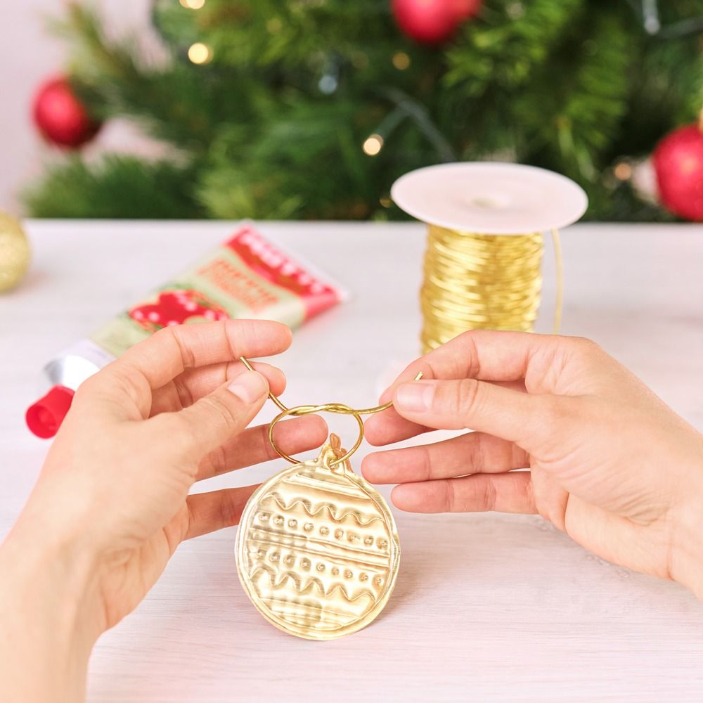 Hands threading golden wire through a clay Christmas ornament