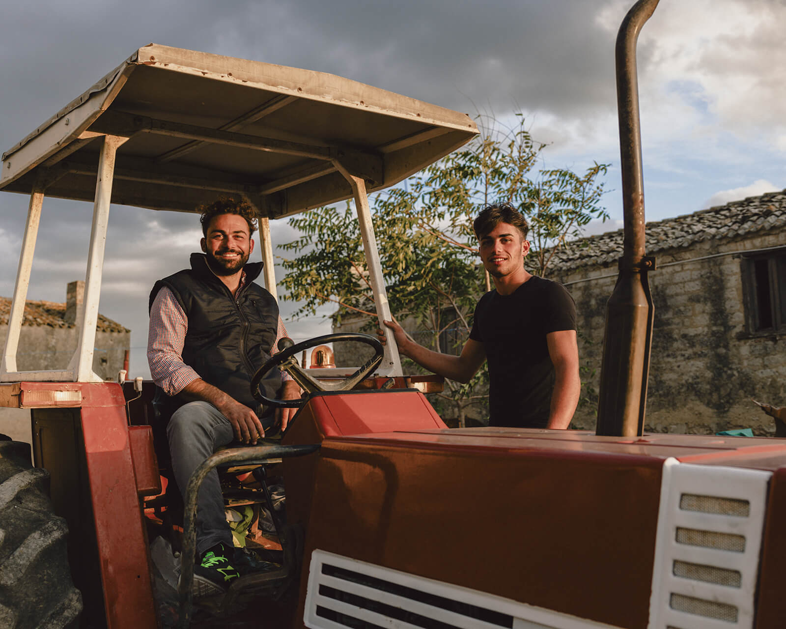 Two young farmers sitting together on a red tractor