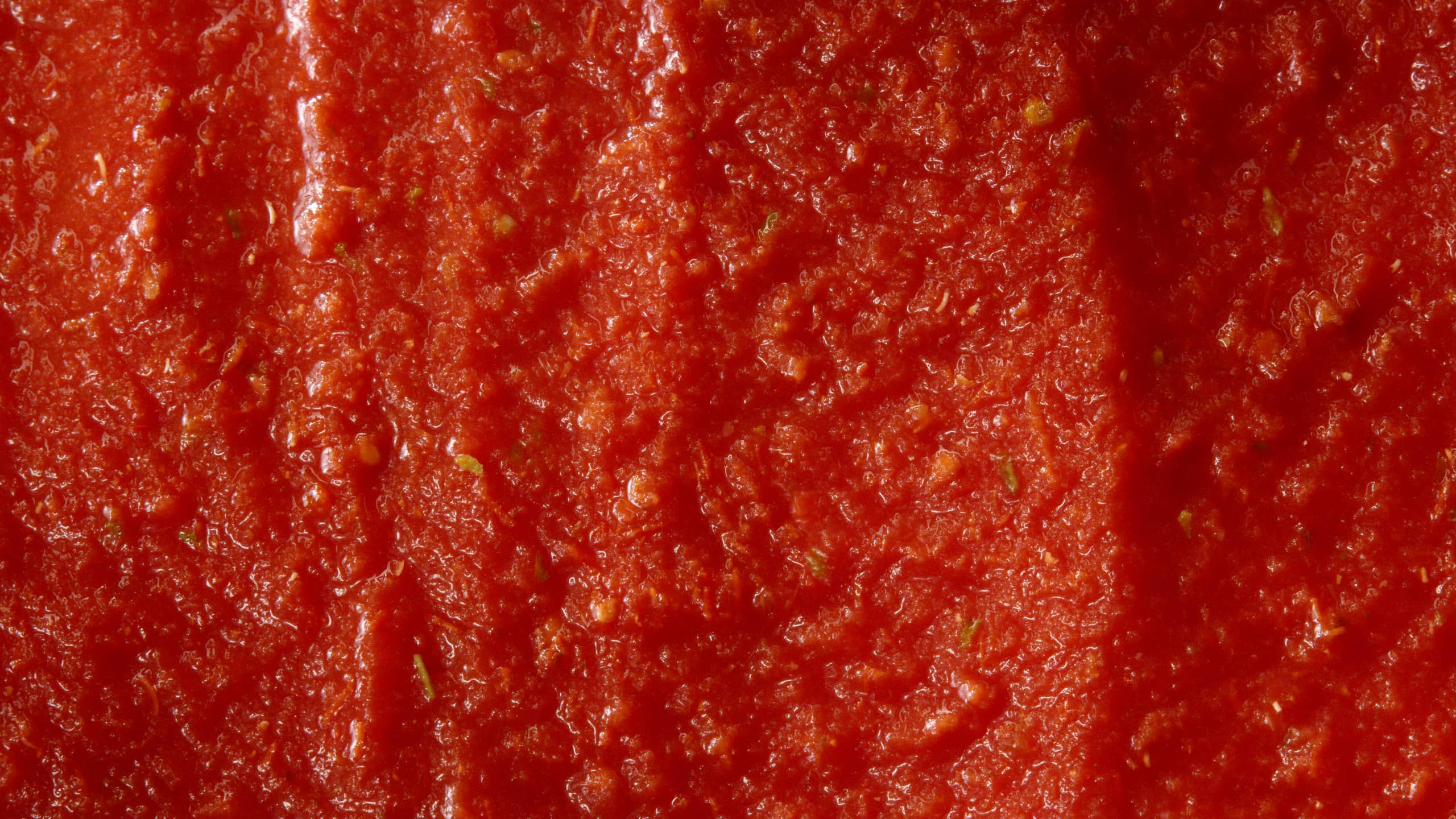 Close-up texture of Mutti pizza sauce with herb flecks