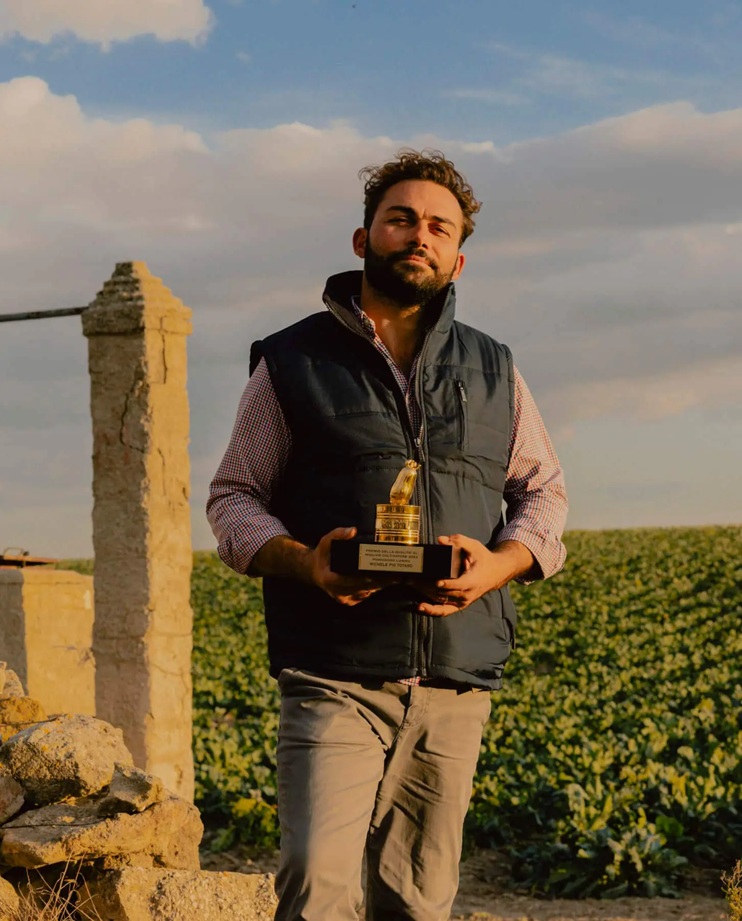Farmer holding the golden Pomodorino d'Oro trophy in a tomato field at sunset